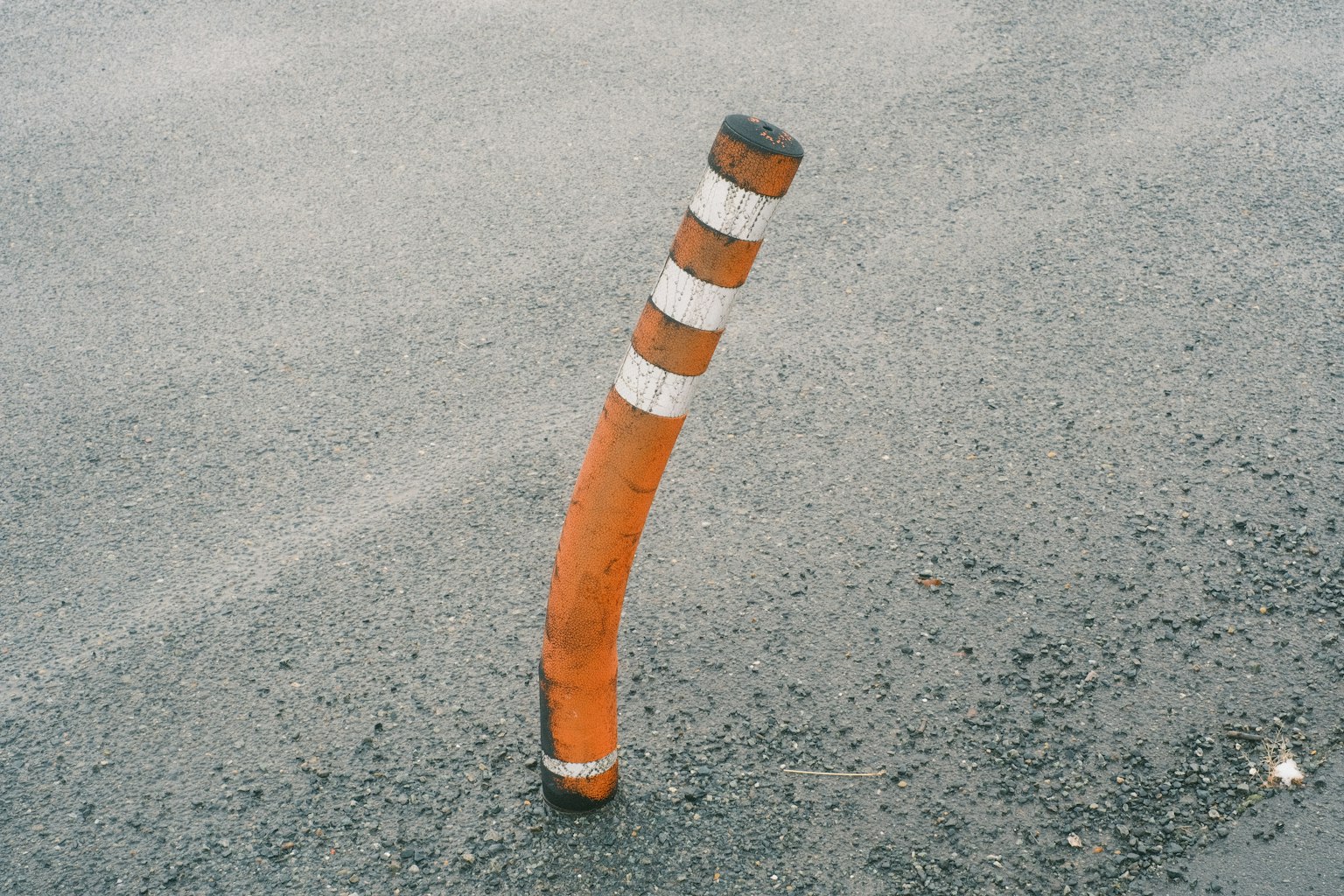 Poste naranja doblado con rayas blancas sobre asfalto