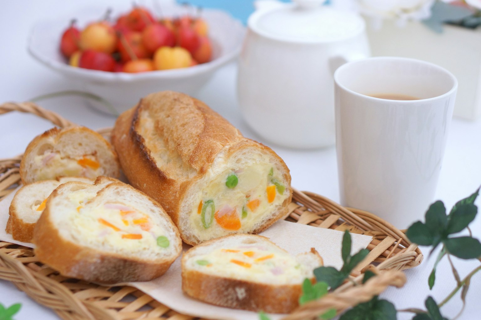 Sliced bread with colorful vegetables on a basket with a bowl of fruit and a cup of tea in the background