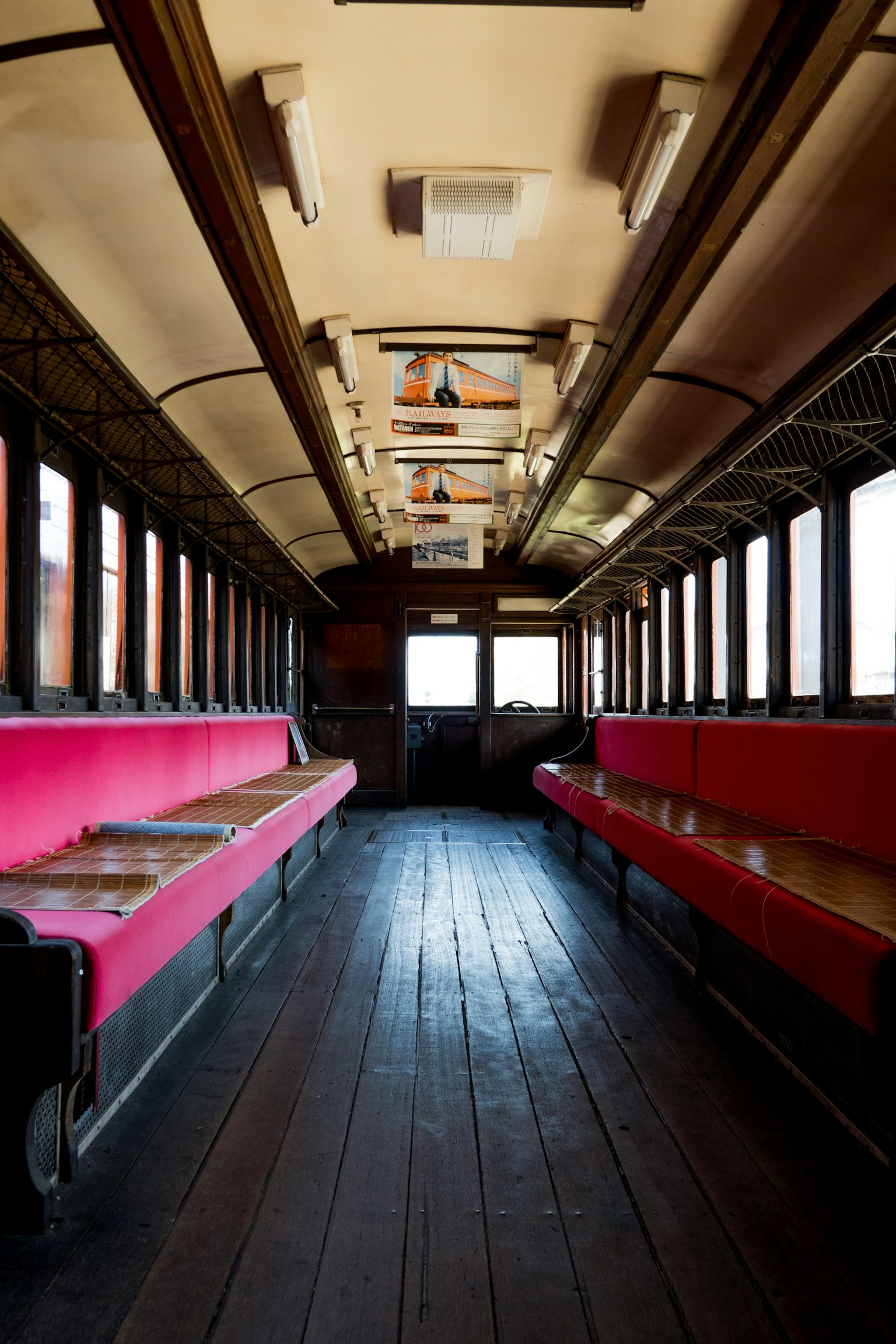 Innenraum eines alten Zugwagens mit roten Bänken und Holzboden