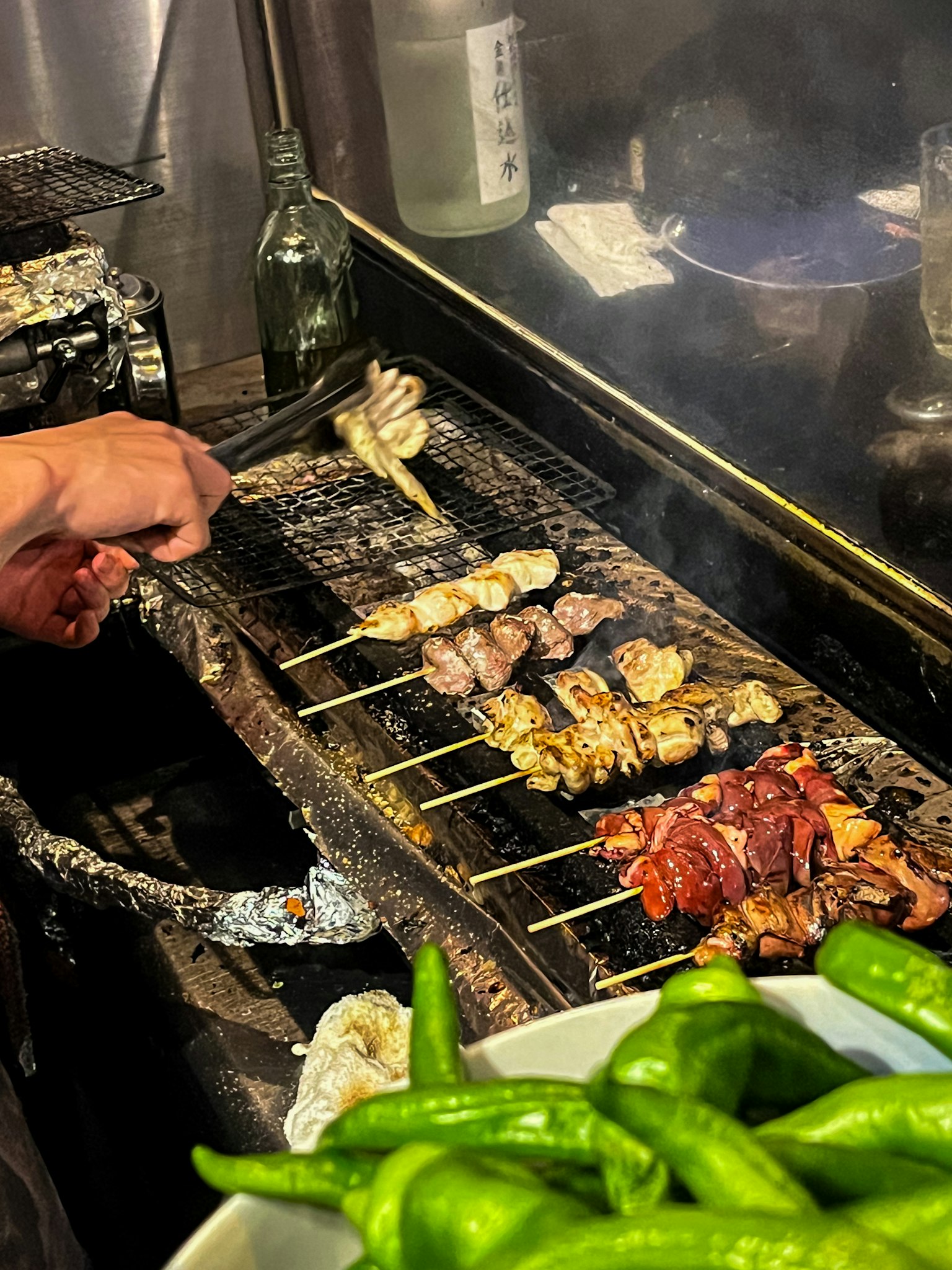 Una mano che griglia spiedini di pollo e peperoni verdi su una griglia