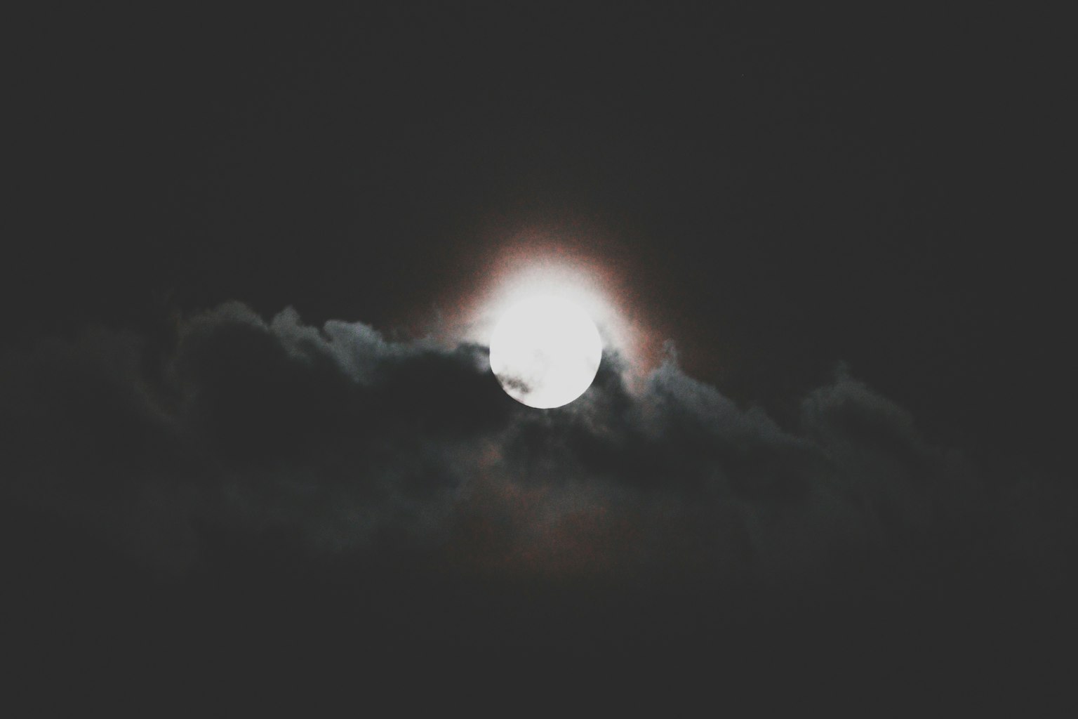 Luna brillante parzialmente coperta da nuvole scure in un cielo notturno