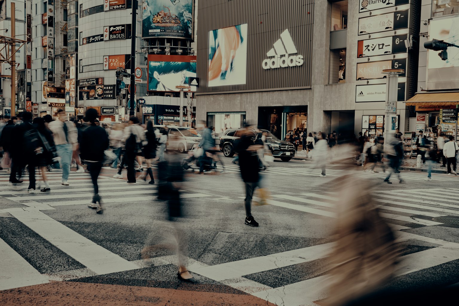 Passanti in un attraversamento pedonale affollato con pubblicità Adidas sullo sfondo