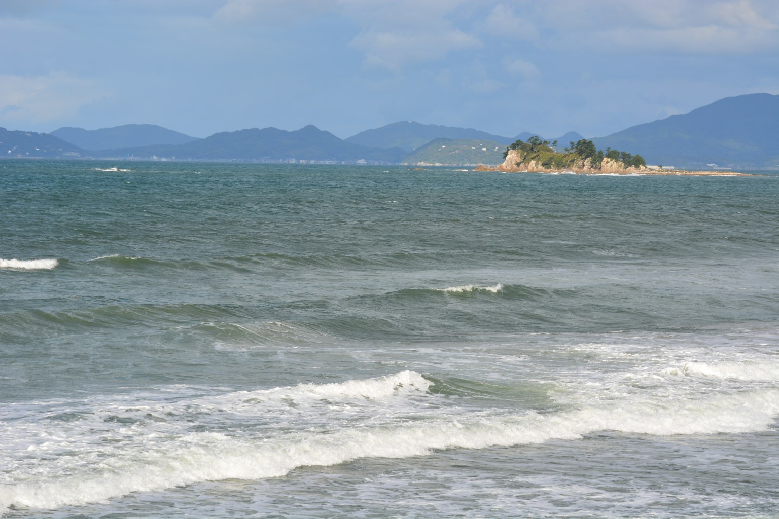 Weitreichender Blick auf das blaue Meer mit Wellen kleine Insel in der Ferne