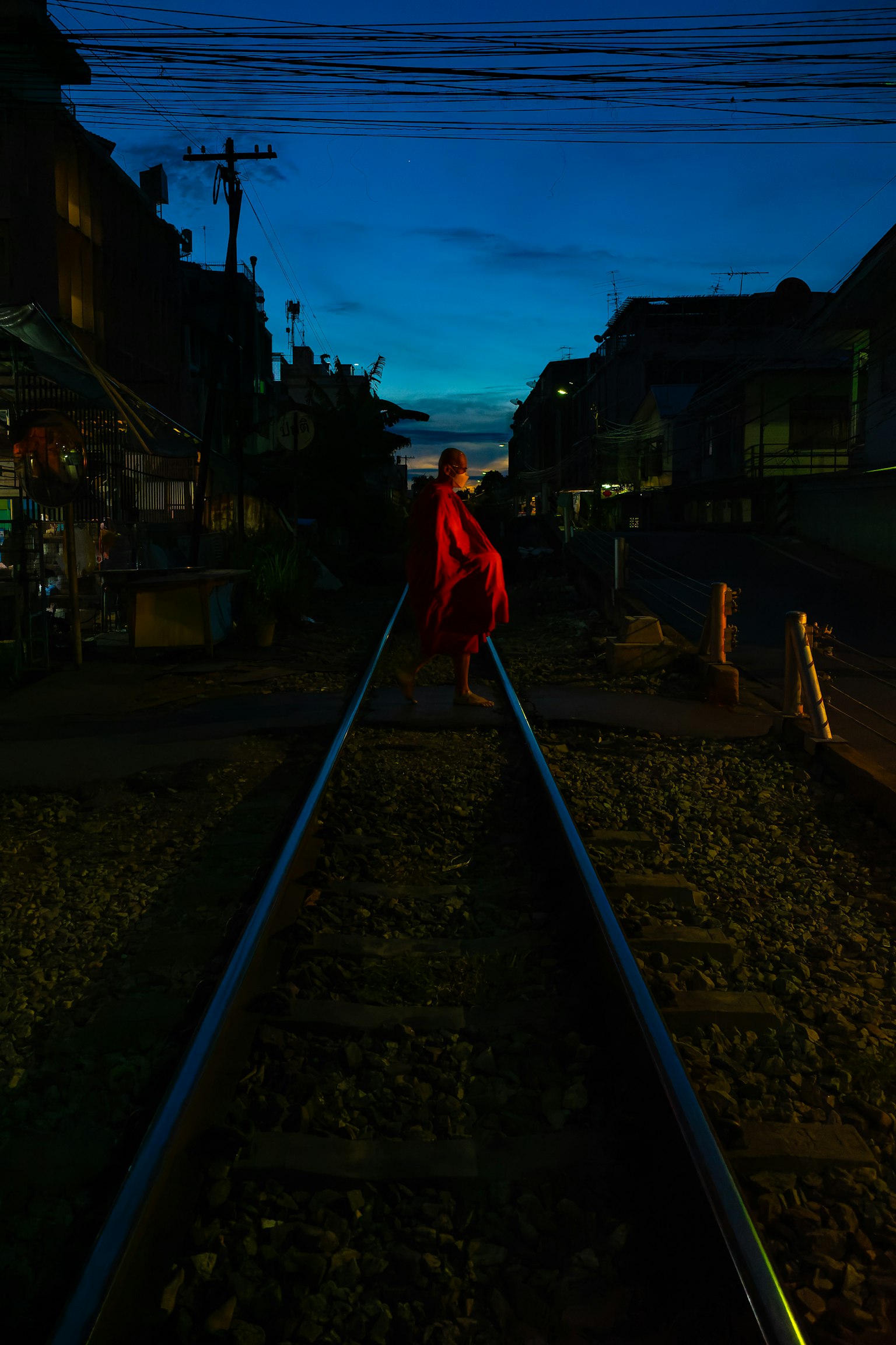 A person in a red outfit standing on train tracks with a twilight background