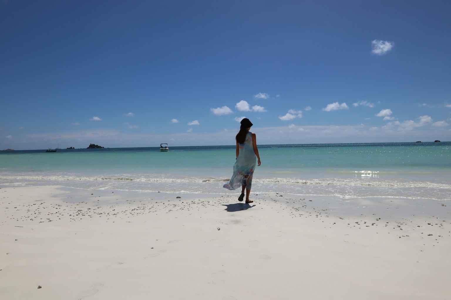 Woman walking on a white sandy beach with blue sea in the background