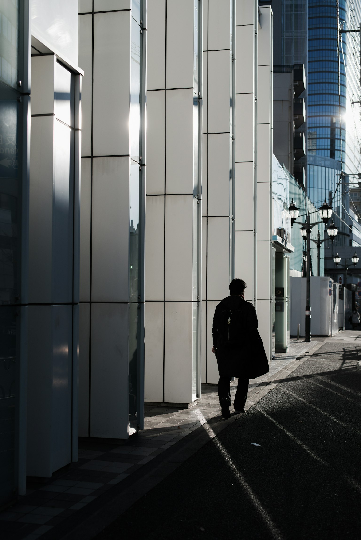 Silhouette of a person walking beside modern buildings reflecting light