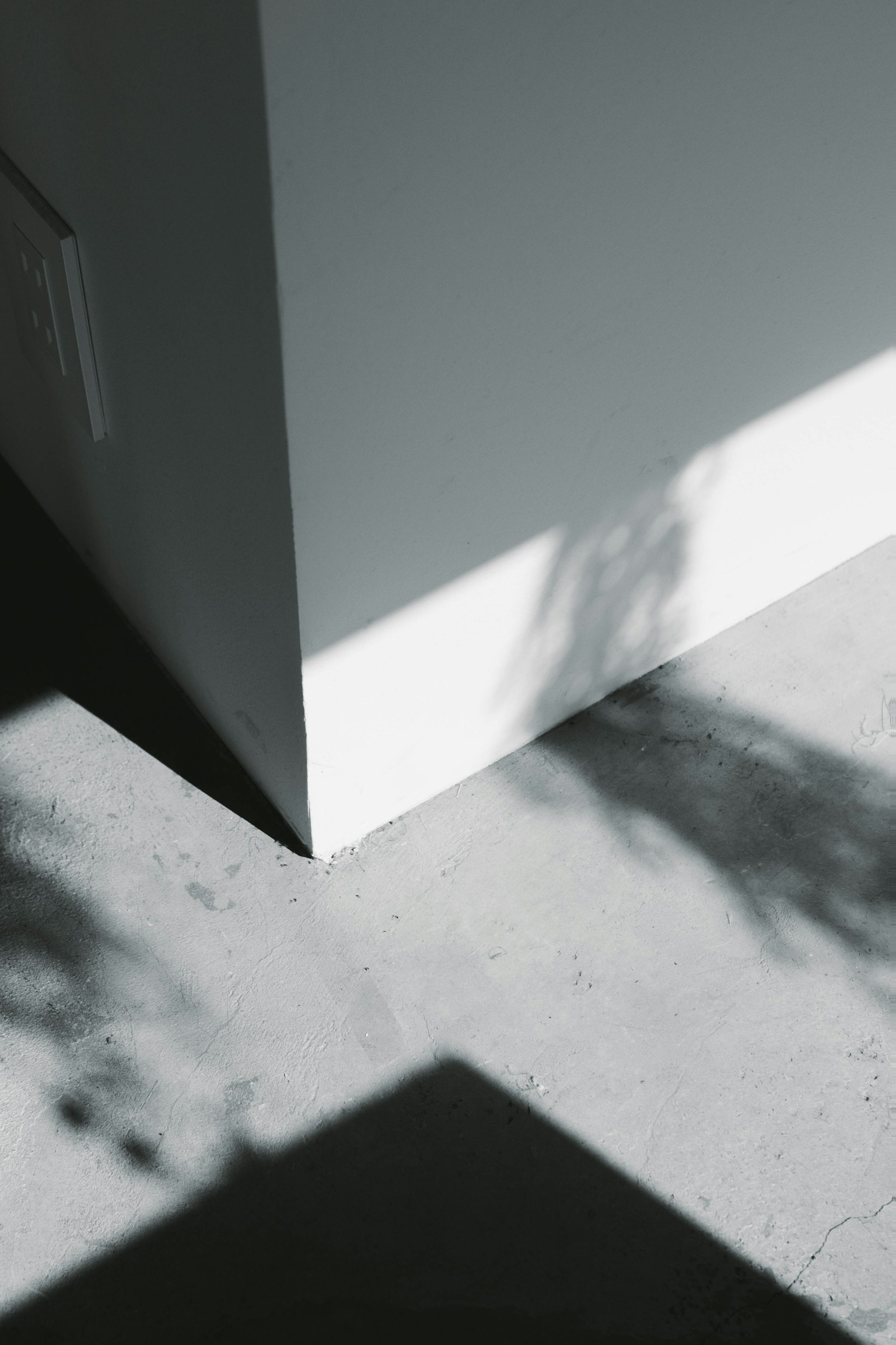 Ecke einer weißen Wand mit kontrastierenden Schatten auf einem Betonboden