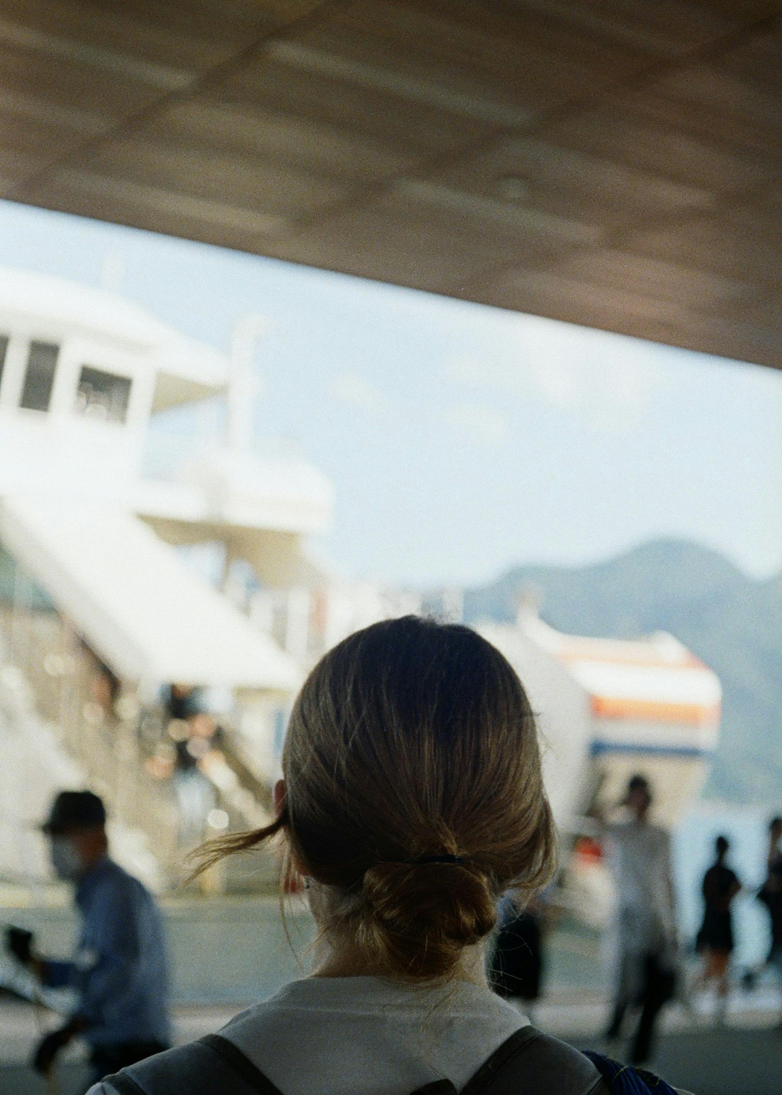 女性が船の乗り場を見つめている風景 背景には船と山々が見える