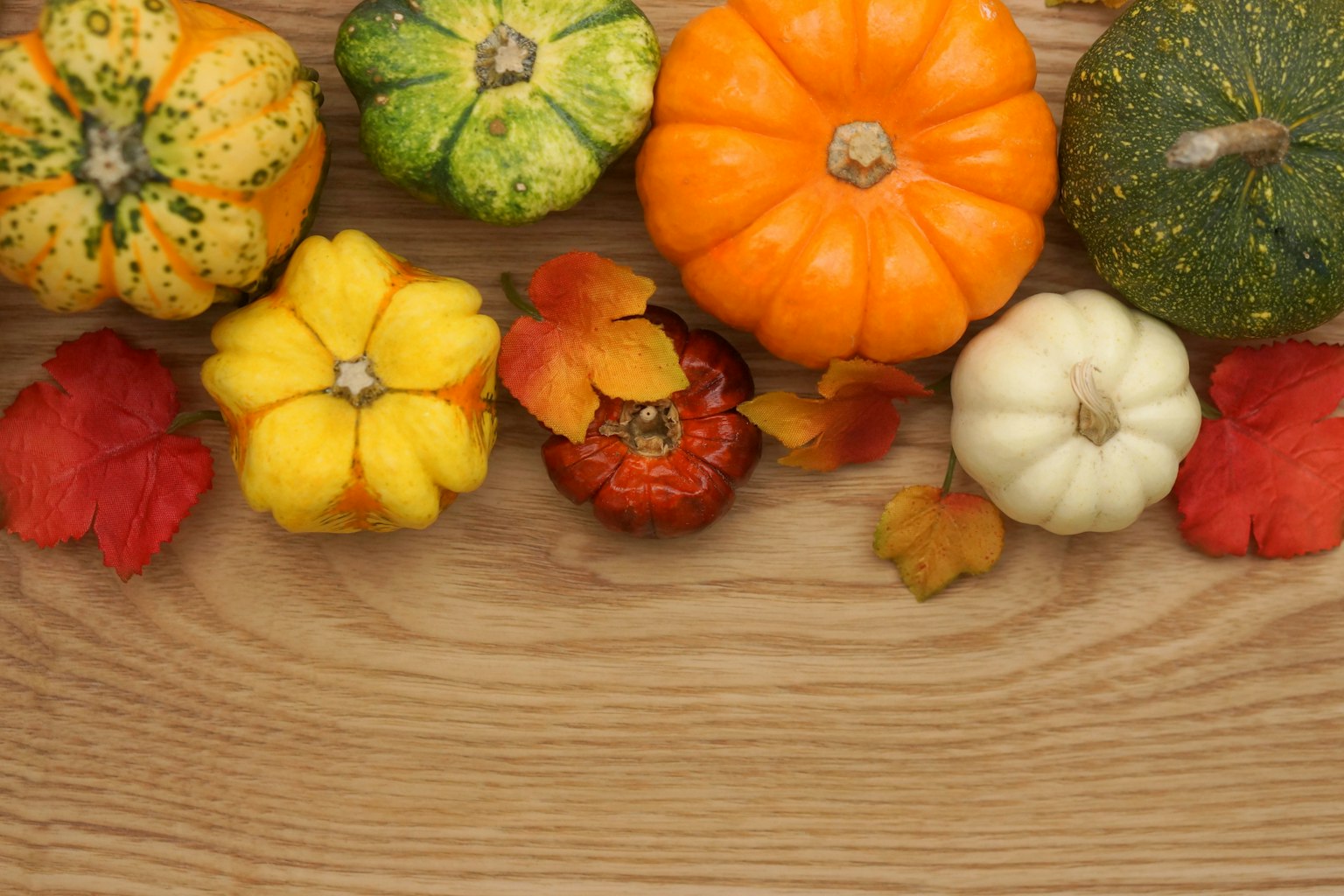 Colorful pumpkins and autumn leaves arranged on a wooden table