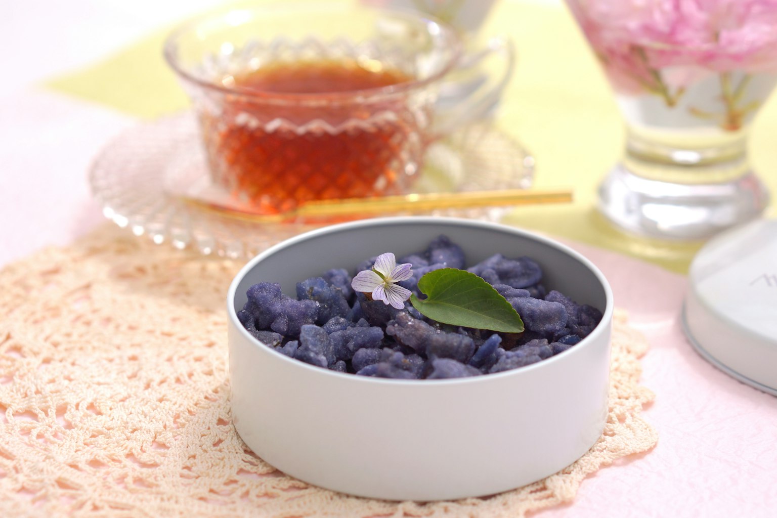 蓝紫色日本甜点在白色碗中，上面有绿叶 茶和花卉装饰在背景中