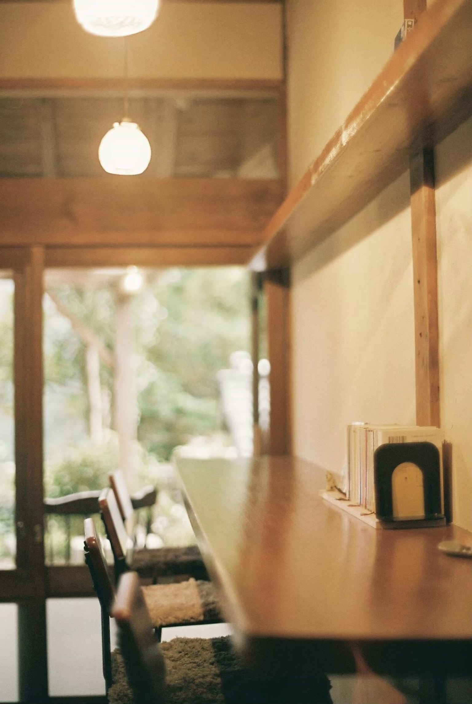 Intérieur de café simple avec un comptoir en bois et des chaises, verdure visible à travers la fenêtre