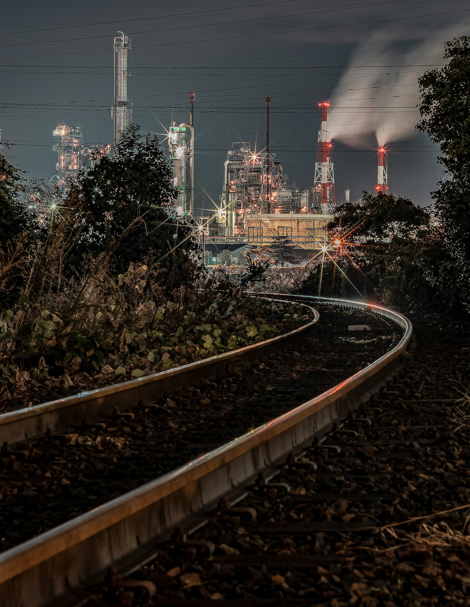 Binario curvo che conduce a un paesaggio industriale di notte