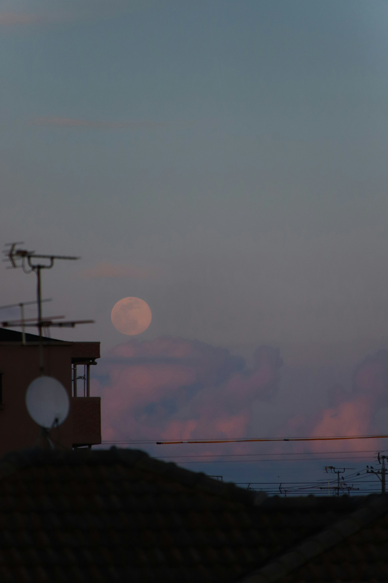 Großer Mond, der in einem farbenfrohen Sonnenuntergangshimmel mit Silhouetten von Dächern aufgeht
