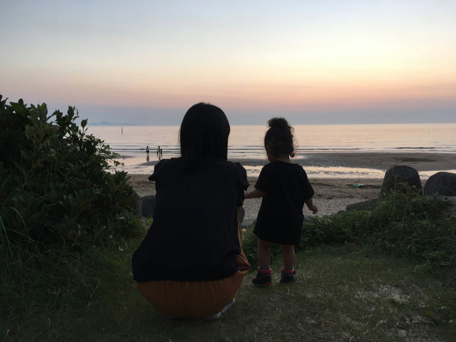 海辺で夕日を見つめる母親と子供のシルエット