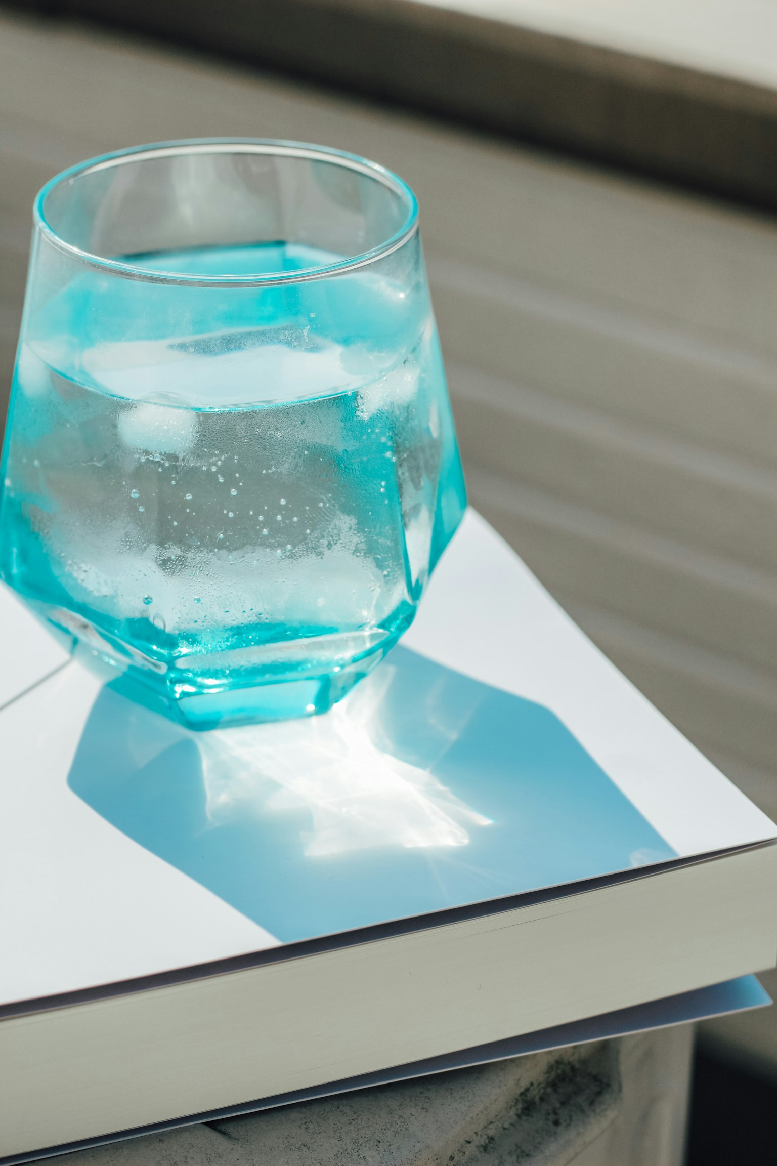 Un verre turquoise rempli d'eau posé sur un livre