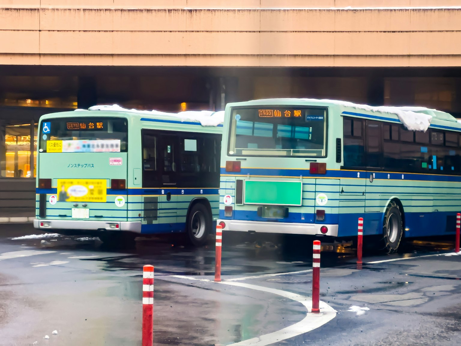 Dos autobuses verdes estacionados en una terminal de autobuses Postes rojos alineados al fondo