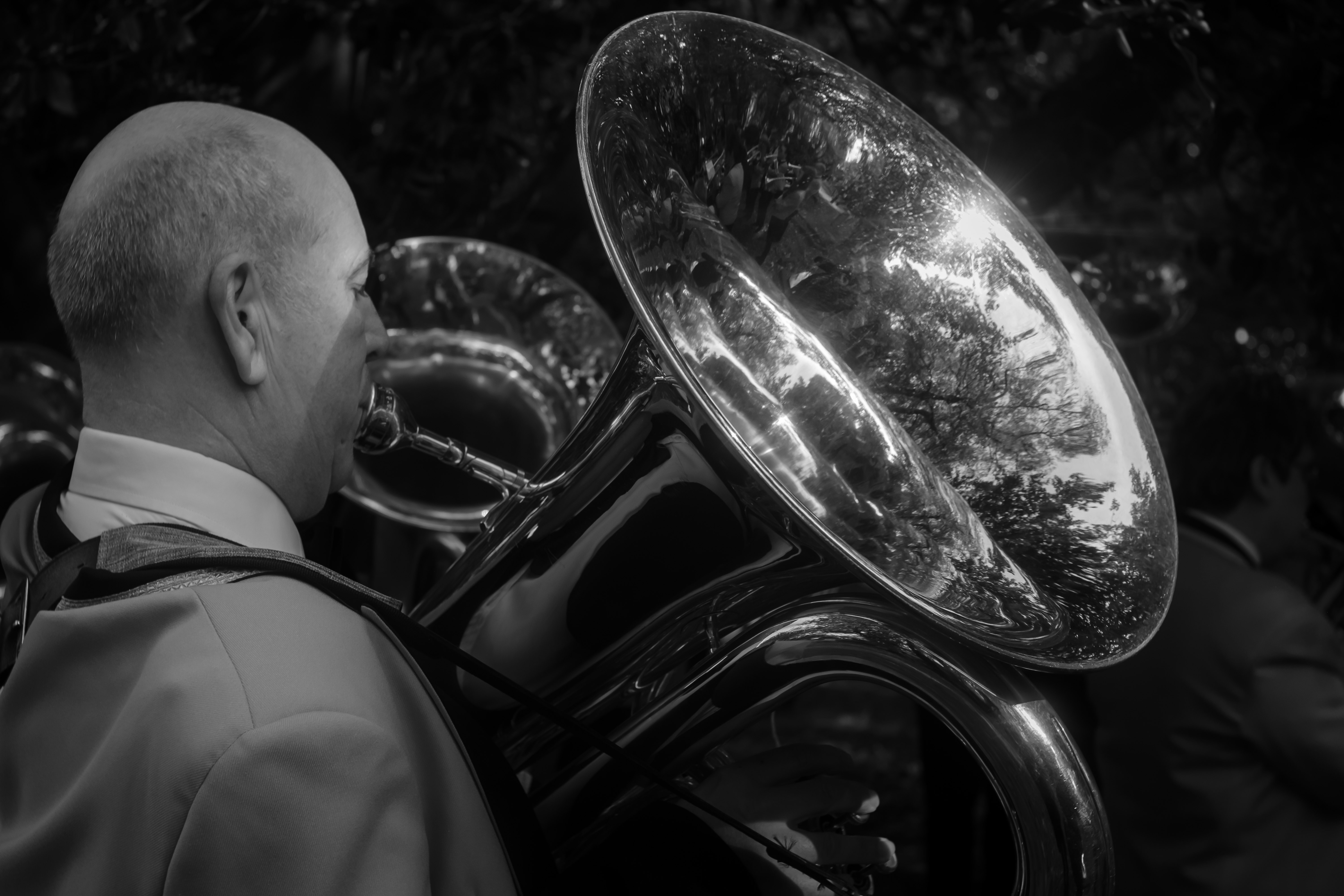 Side profile of a musician with a tuba’s metal bell against a dark background