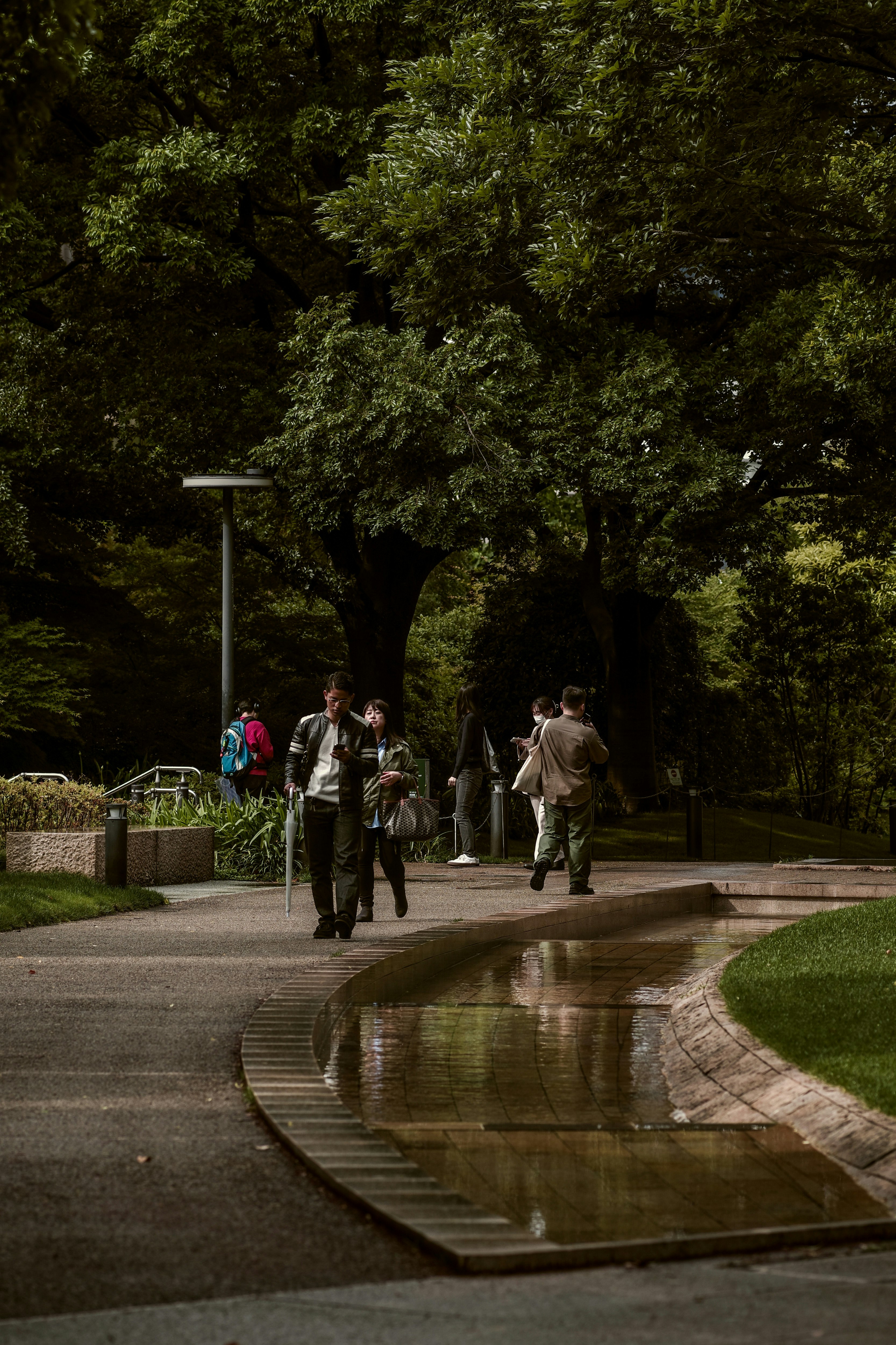 小川のある公園の小道を歩く人々のある風景