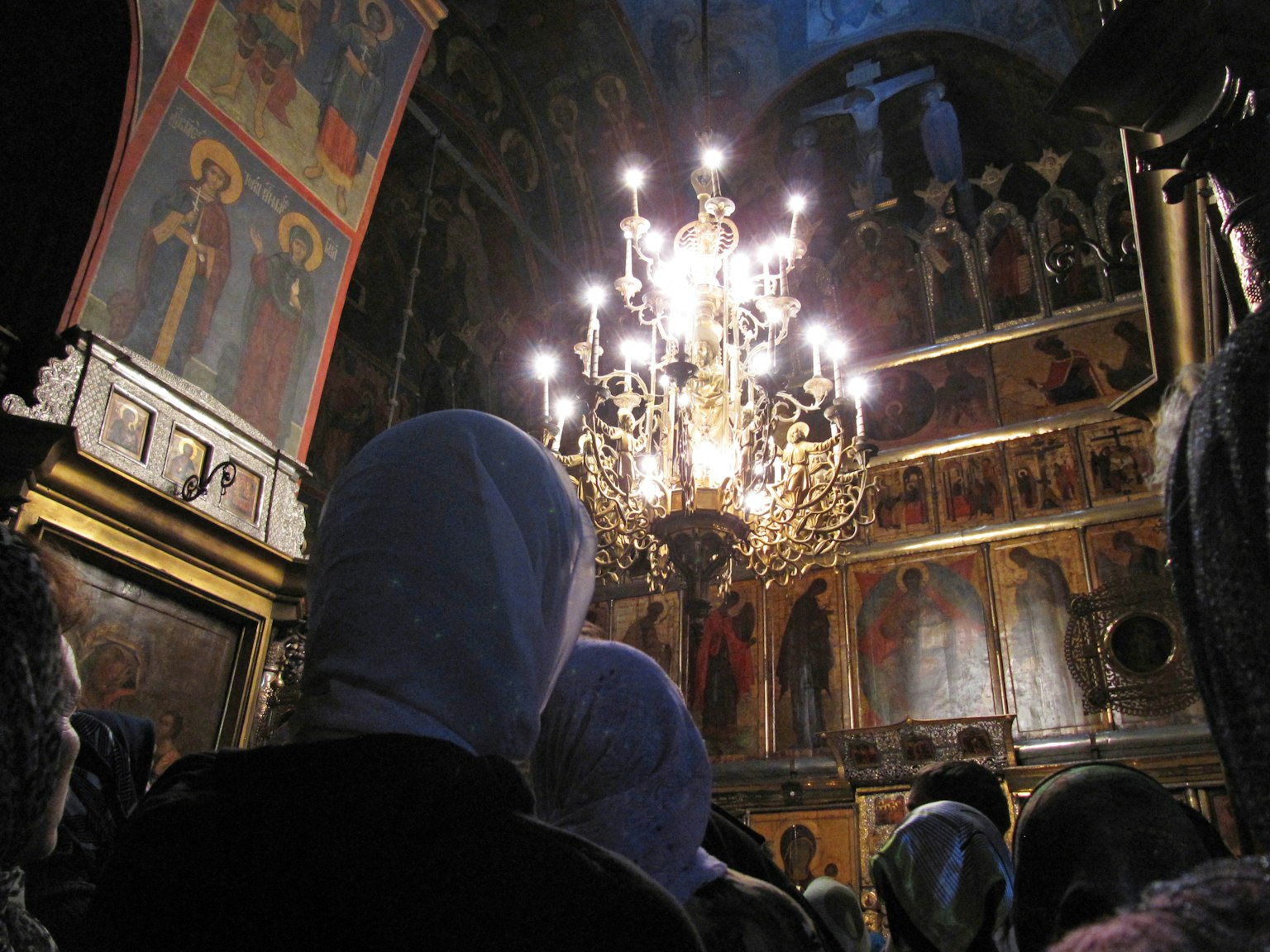 Interior of a church with people wearing headscarves gathered, chandelier lights illuminating the space