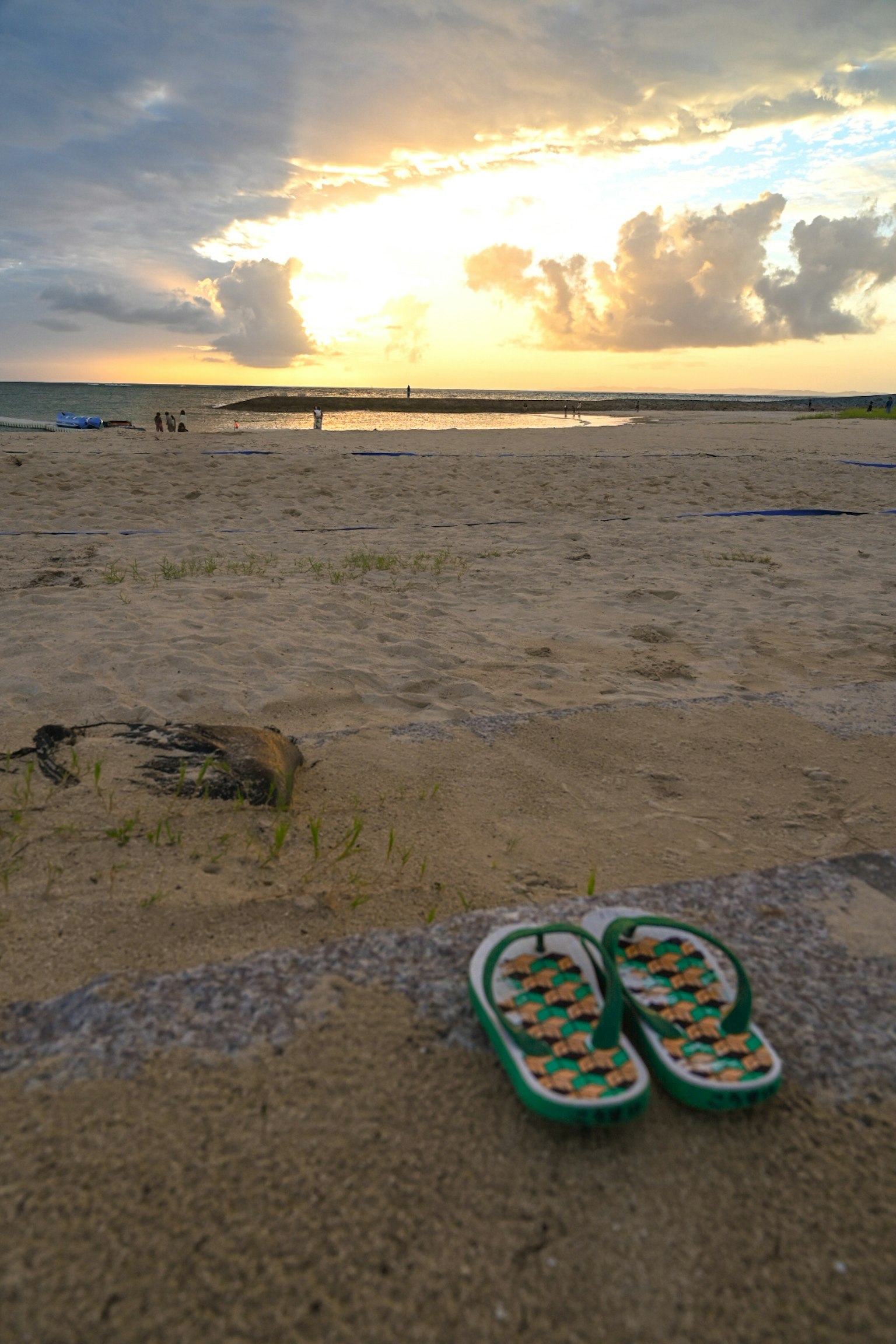 Sandales de plage posées sur le sable avec le coucher de soleil en arrière-plan