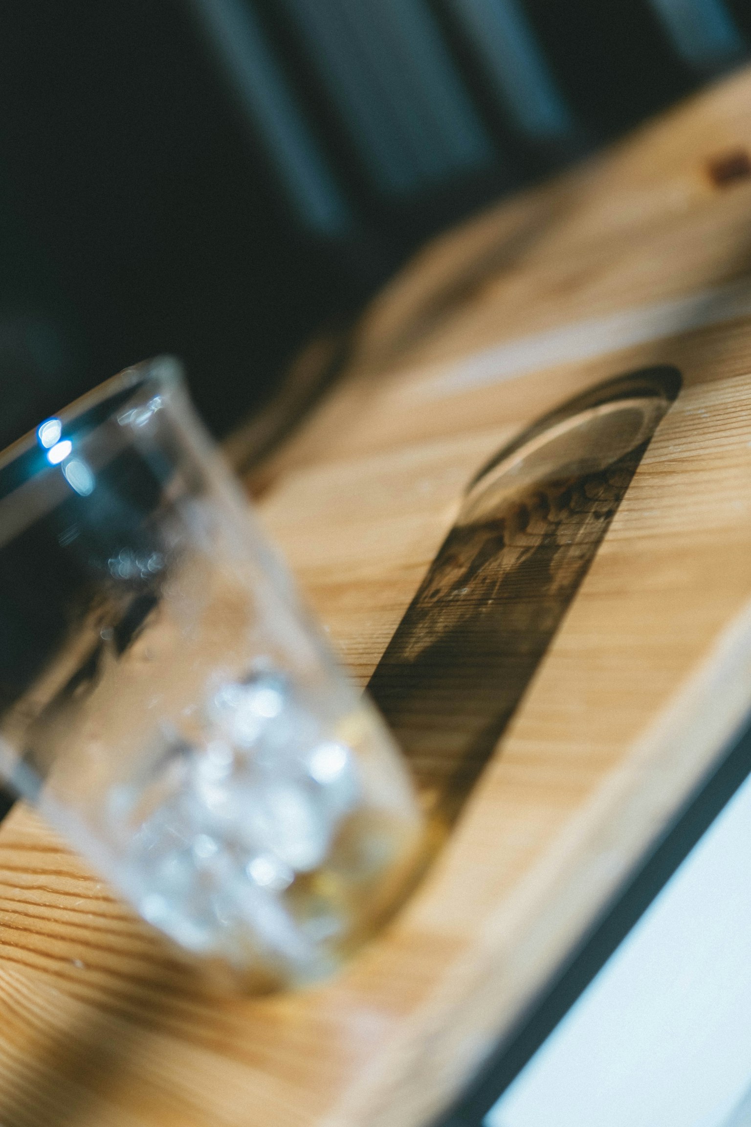 Vaso transparente con hielo sobre una mesa de madera proyectando una sombra