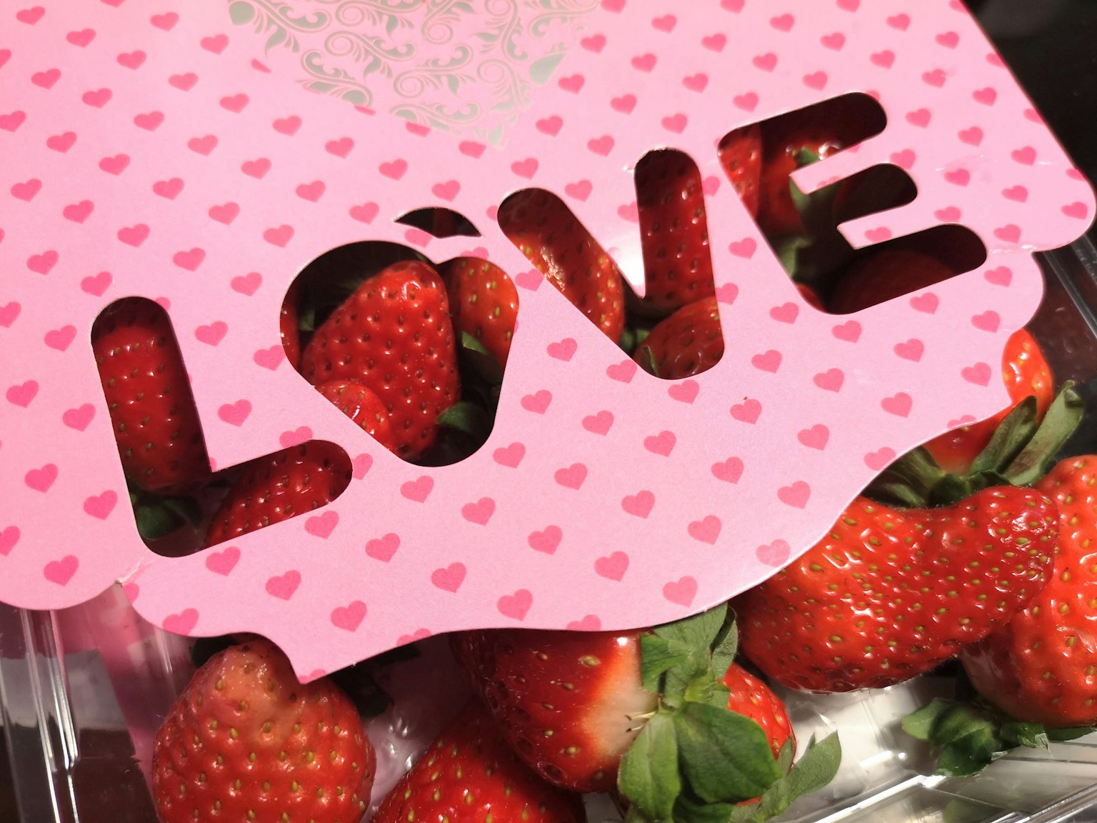Pink packaging with the word LOVE cut out revealing fresh strawberries