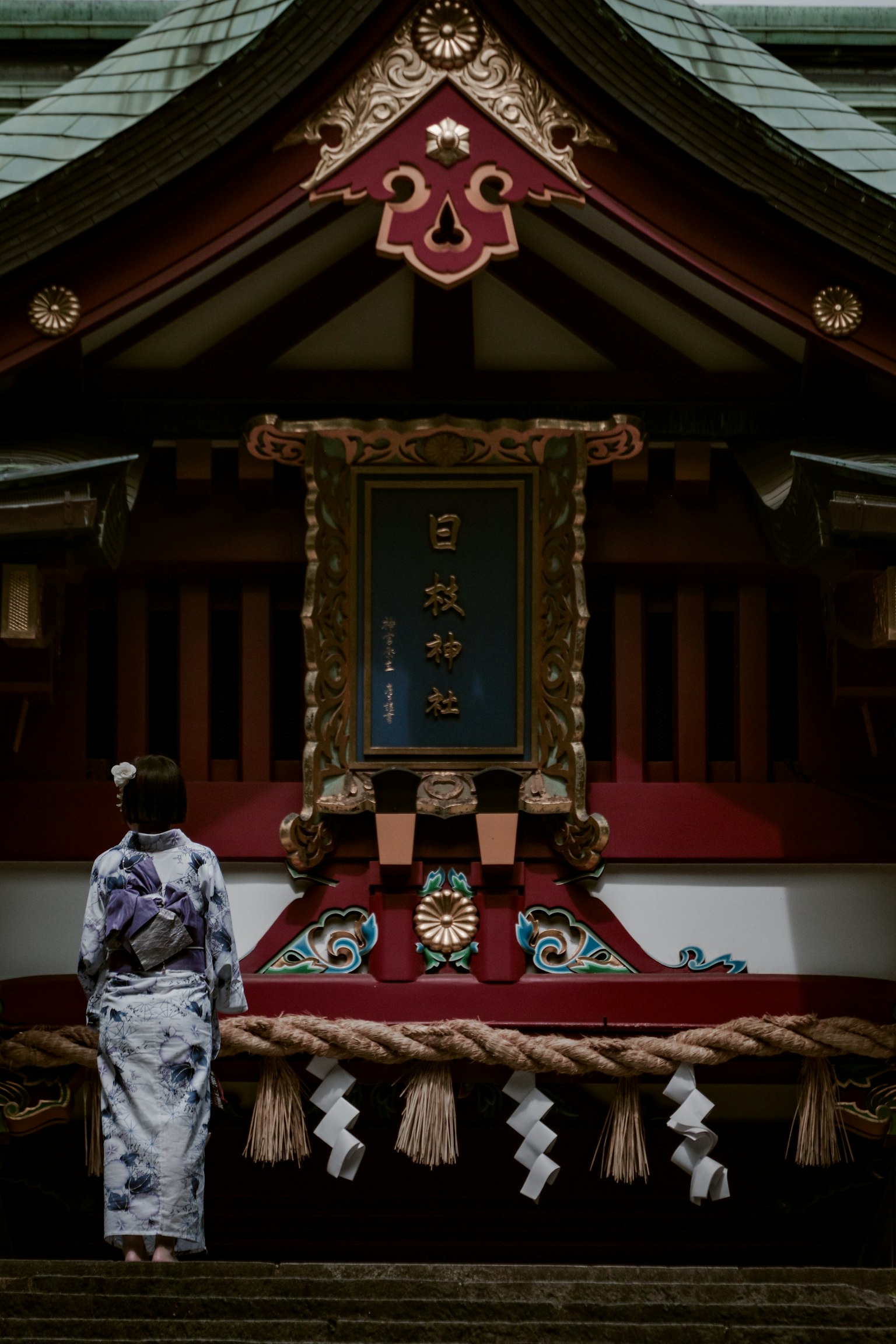 ผู้หญิงในชุดกิโมโนแบบดั้งเดิมยืนอยู่หน้าศาลเจ้าที่มีการตกแต่งที่ประณีตและบรรยากาศศักดิ์สิทธิ์
