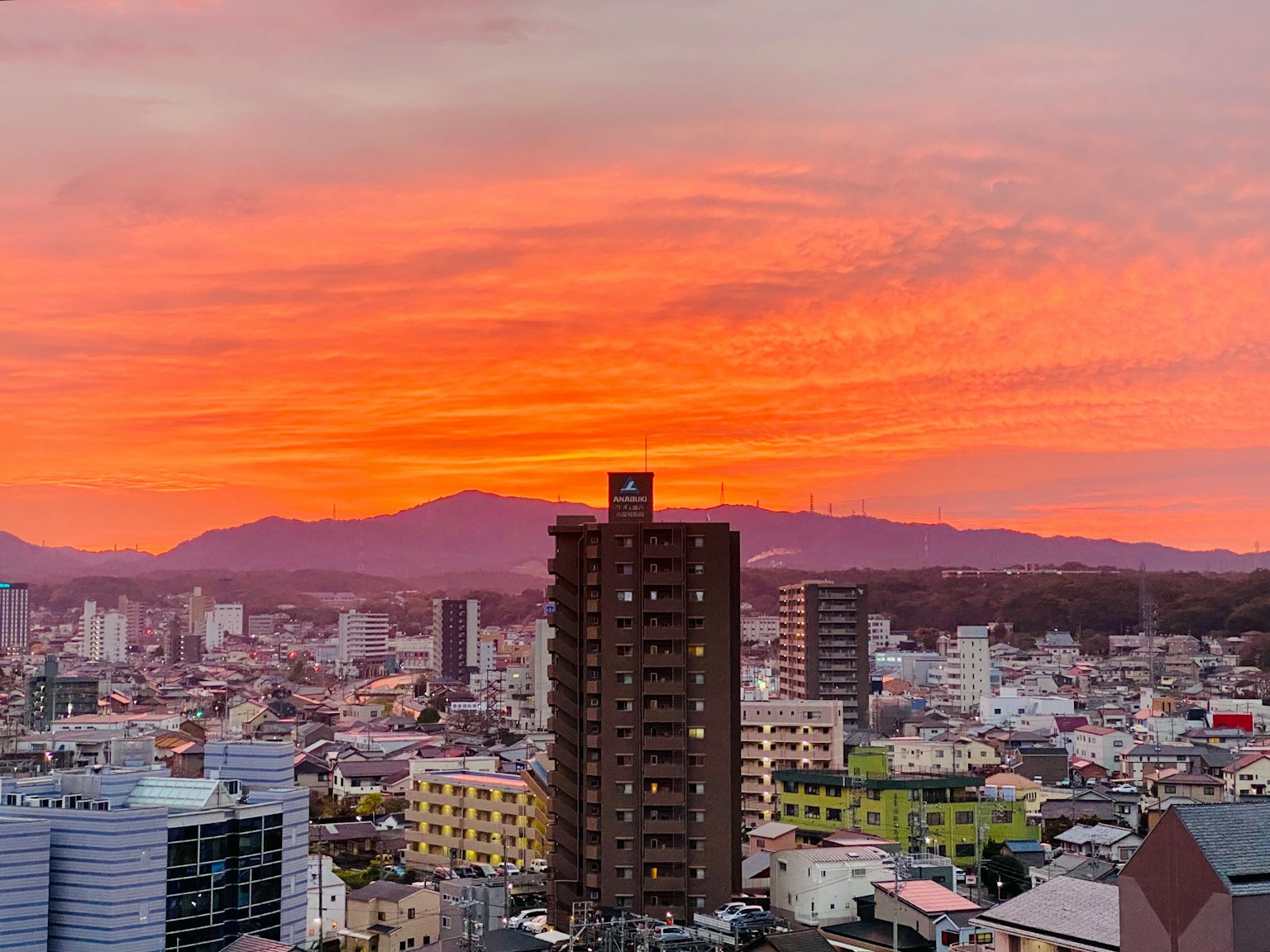 Paysage urbain au coucher du soleil avec un ciel orange vif et des silhouettes de montagnes