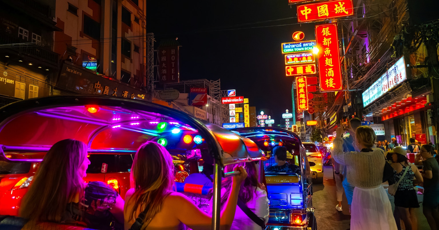 Jalan ramai di malam hari dengan papan neon dan tuk-tuk berwarna-warni
