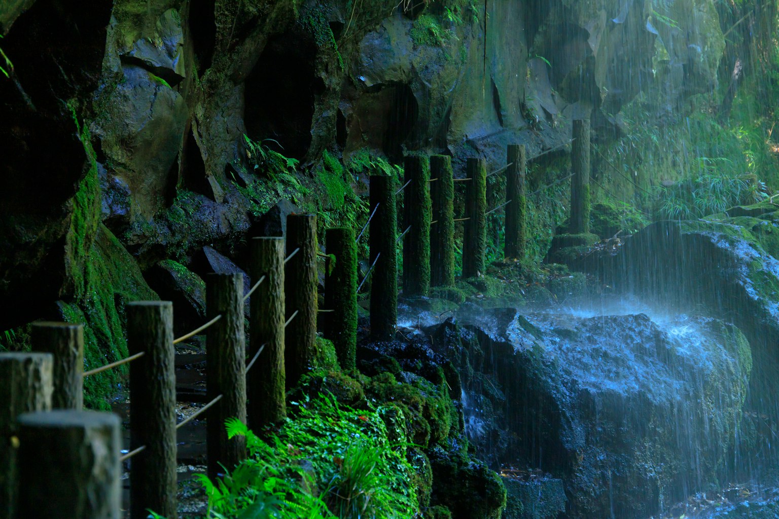 Rambarde en bois à côté d'un mur de roche couvert de mousse et d'une petite cascade