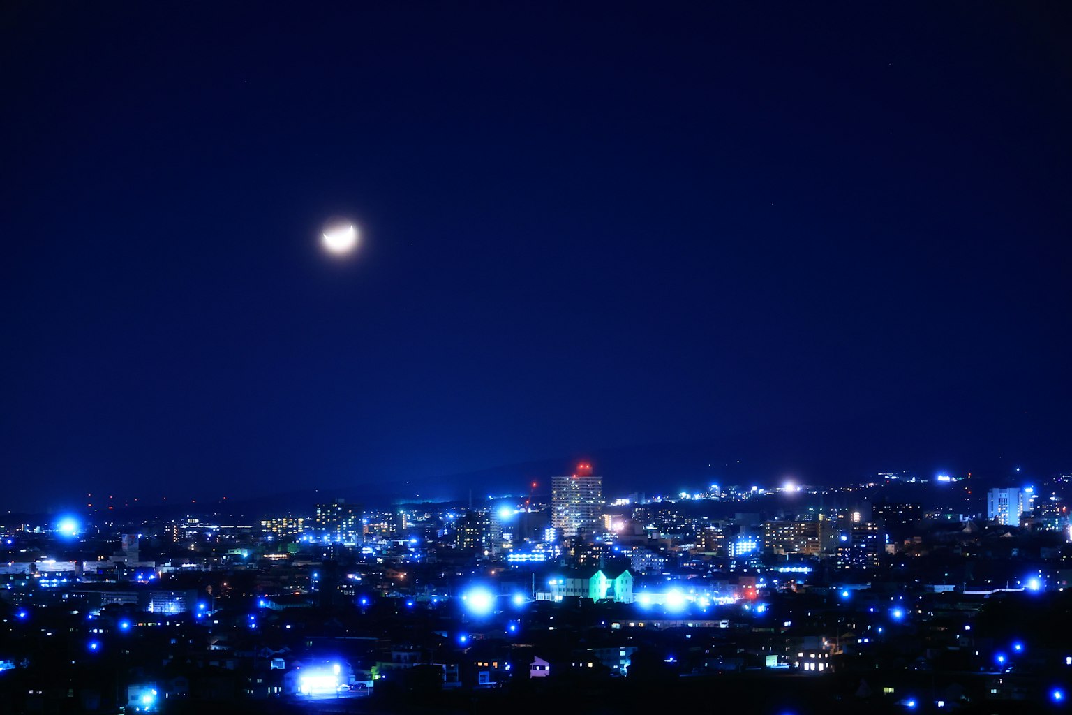 Pemandangan kota malam yang diterangi cahaya biru dengan bulan purnama