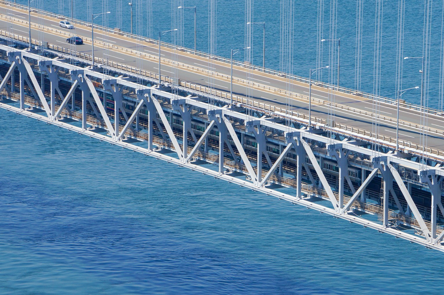 Jembatan modern yang membentang di atas air biru dengan kendaraan di jalan