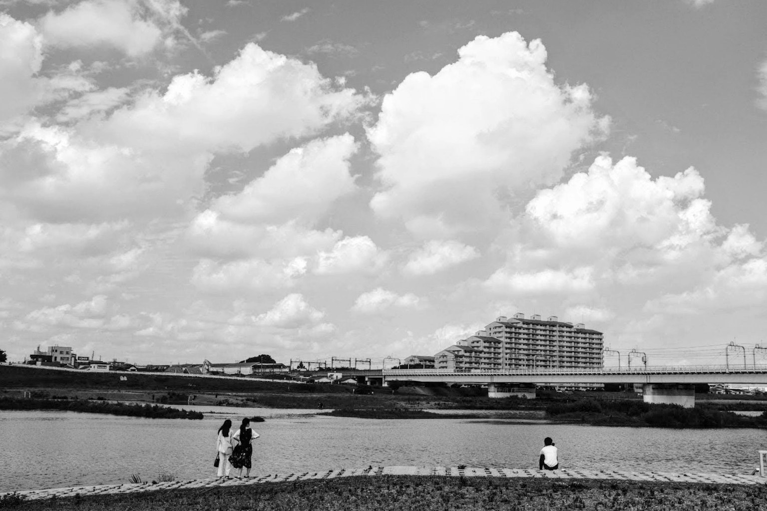 Cảnh quan đen trắng với con sông và tòa nhà cao dưới bầu trời có người ngồi