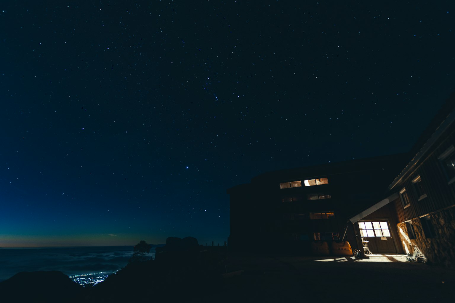 Silhouette d'une cabane avec de la lumière passant par les fenêtres sous un ciel étoilé