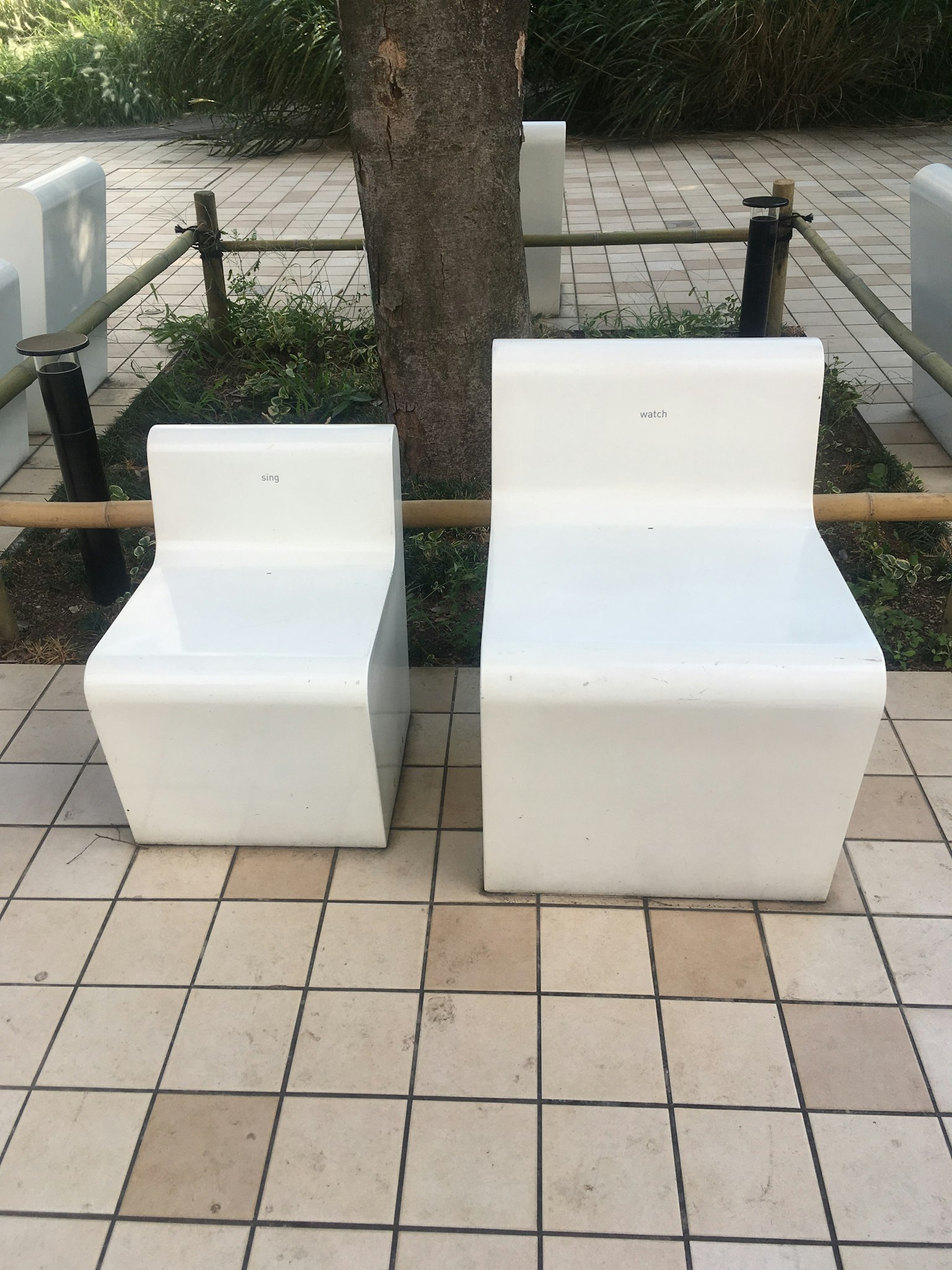 Two modern white chairs with a minimalist design placed on tiled pavement