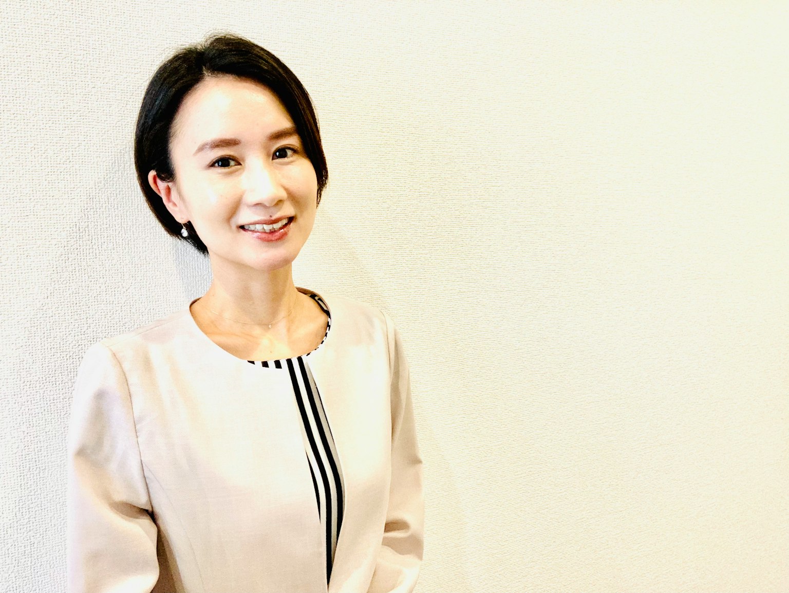 Một người phụ nữ đứng trước nền sáng mặc trang phục sáng màu và mỉm cười
