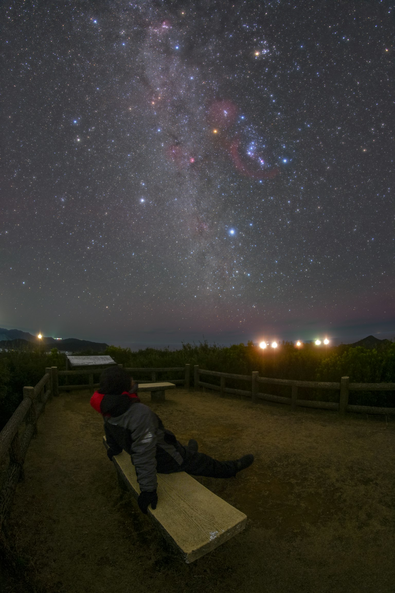 Person sitting on a bench under a starry sky with the bright Milky Way