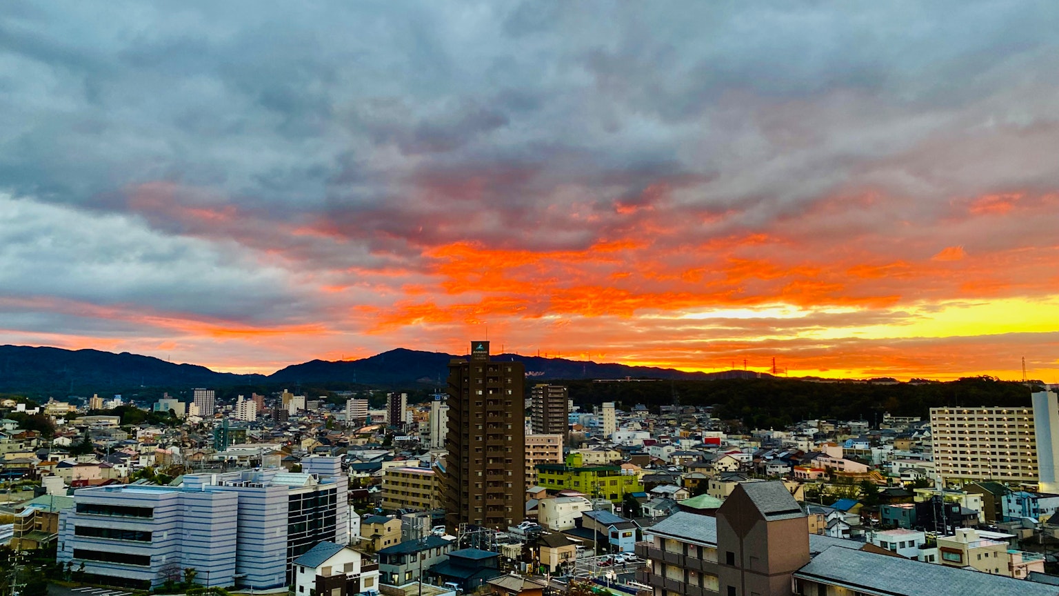 Panorama urbain au coucher du soleil avec des nuages colorés et une silhouette de montagne