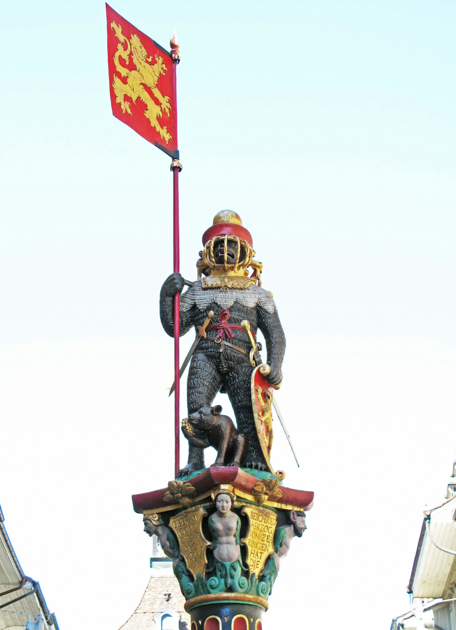 Une statue de chevalier tenant un drapeau de lion se dresse au sommet d'une haute colonne