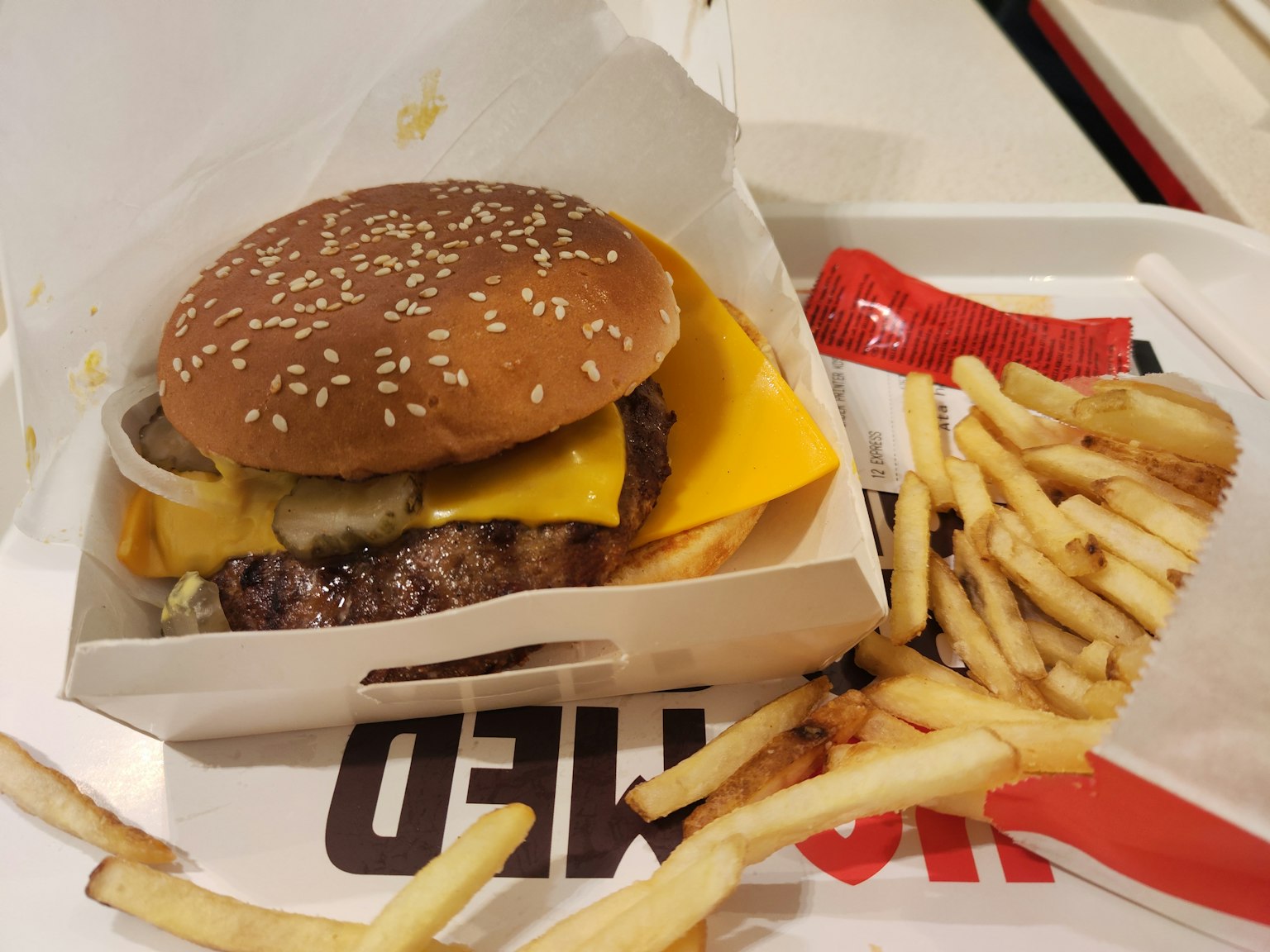 Burger with sesame bun and fries in a takeout box