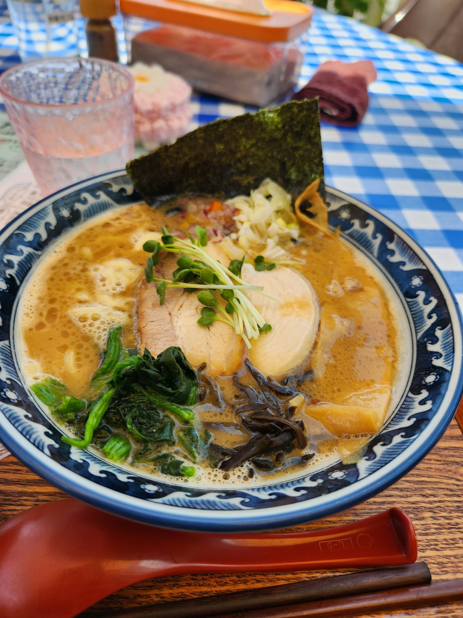 一碗拉面，上面放着猪肉片、海苔和蔬菜