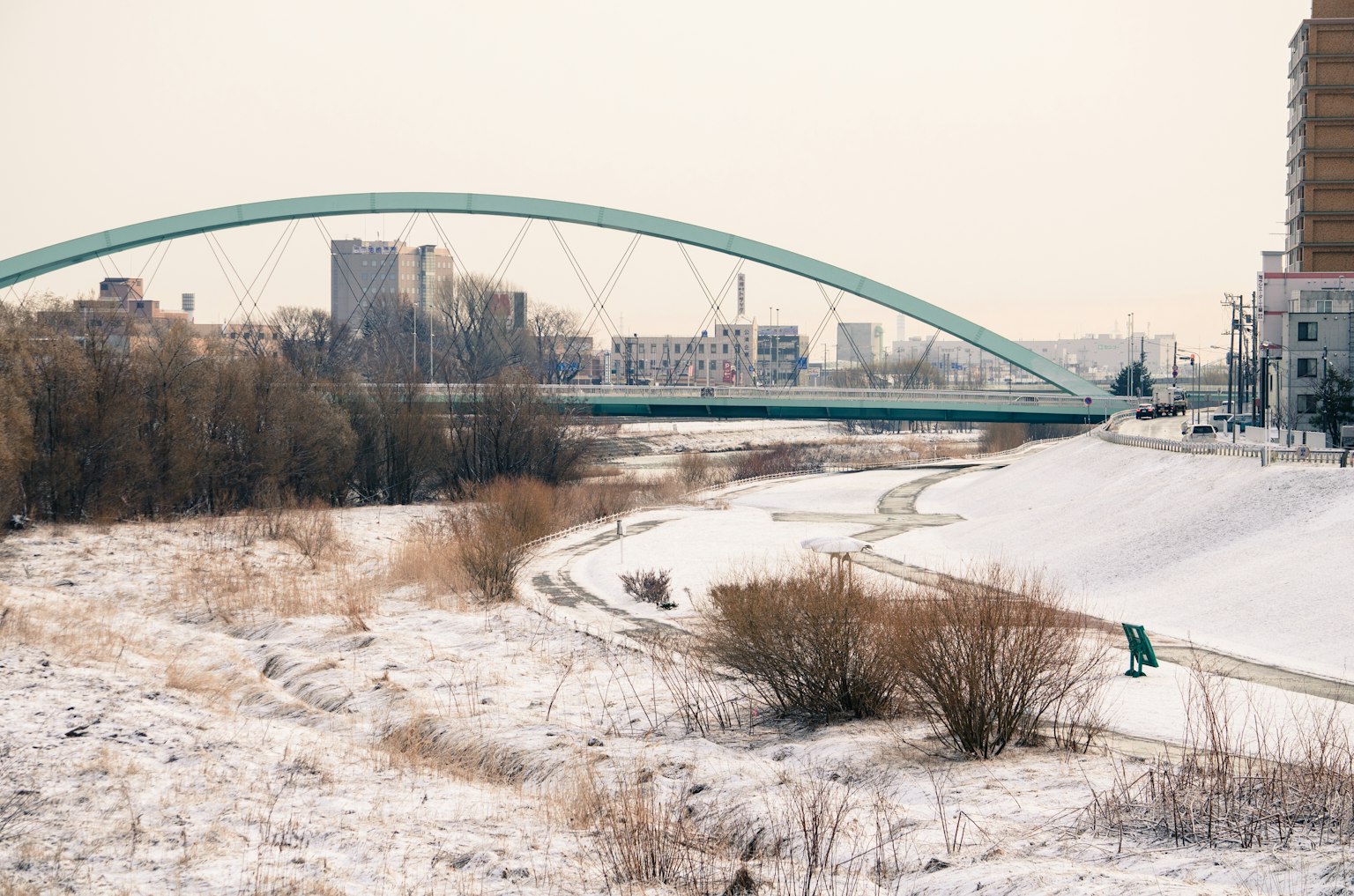 Winter scene featuring a snow-covered river and a green arch bridge