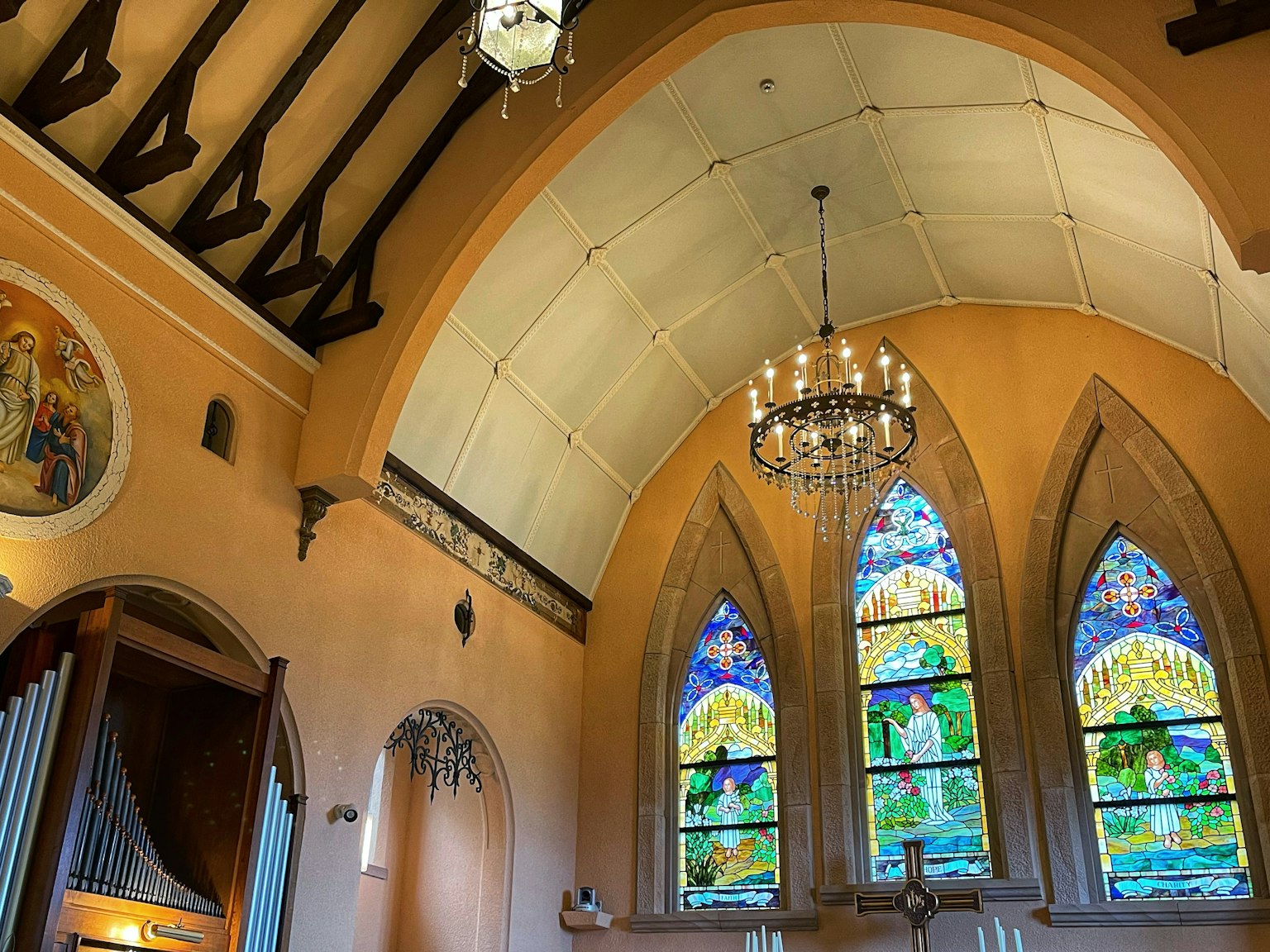 Interior gereja dengan jendela kaca patri berwarna langit-langit kayu dan lampu gantung