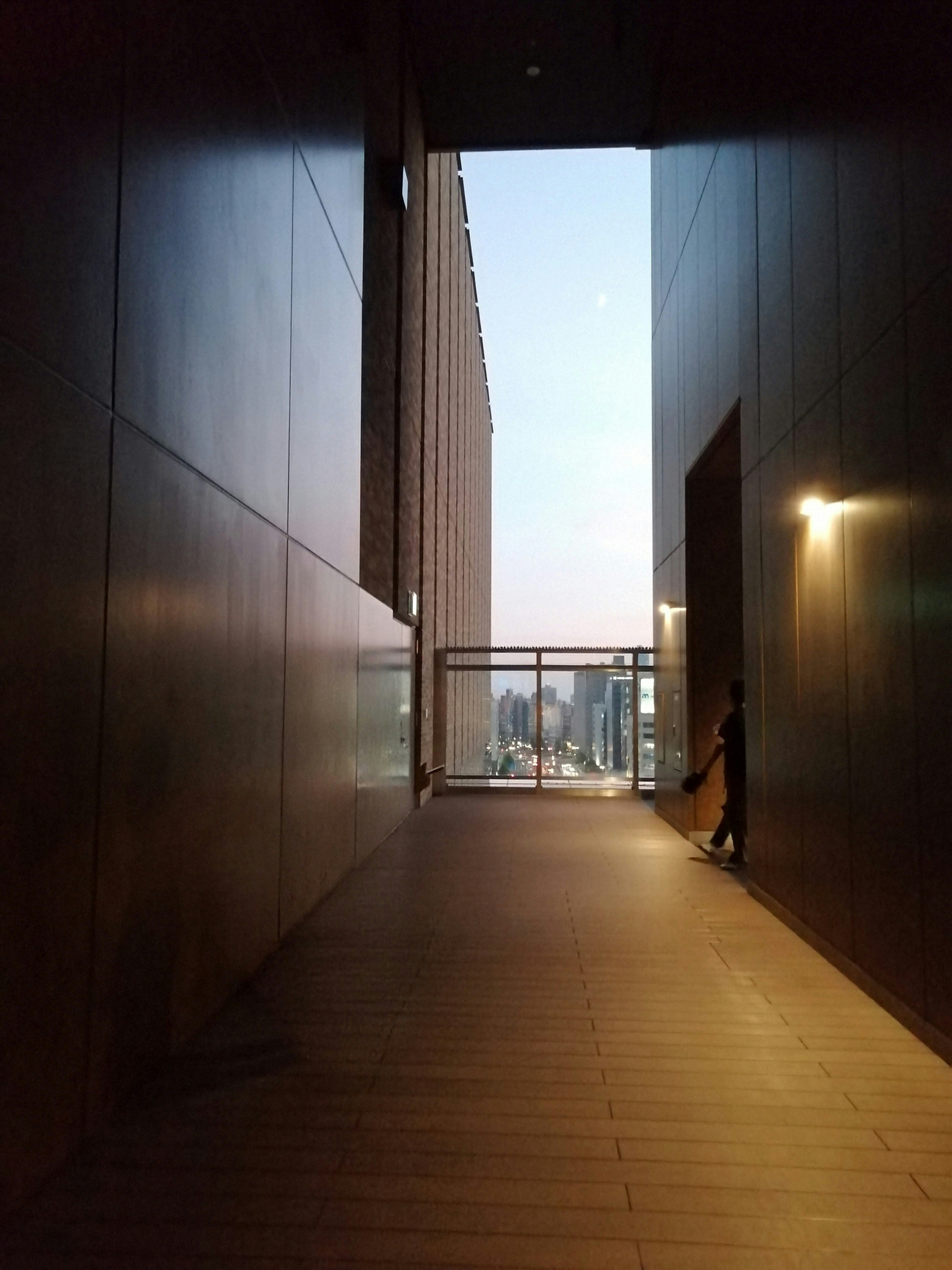 壁に挟まれた通路の奥に差し込む光と人影のある街の風景
