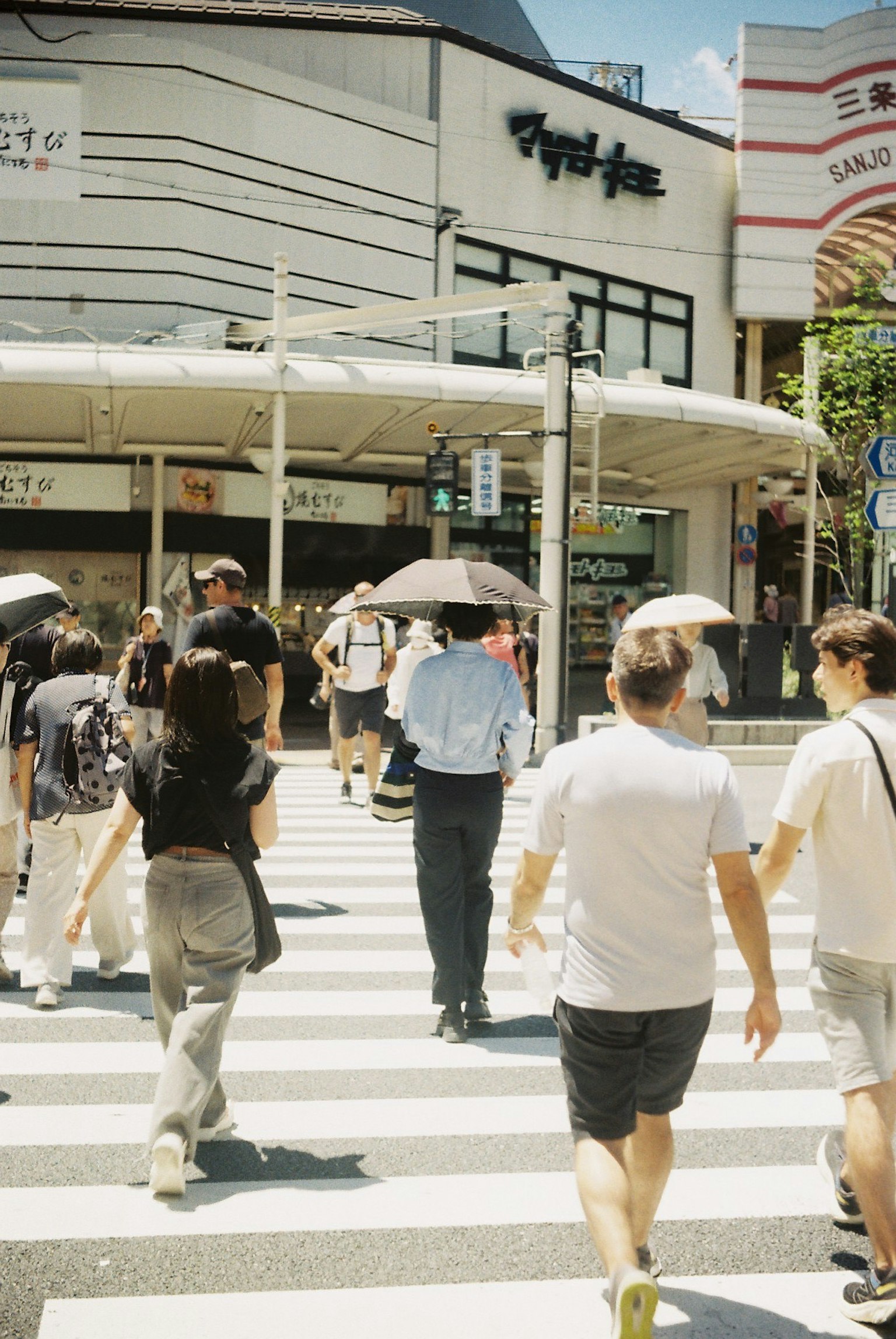 People crossing a busy intersection while using umbrellas for sun protection