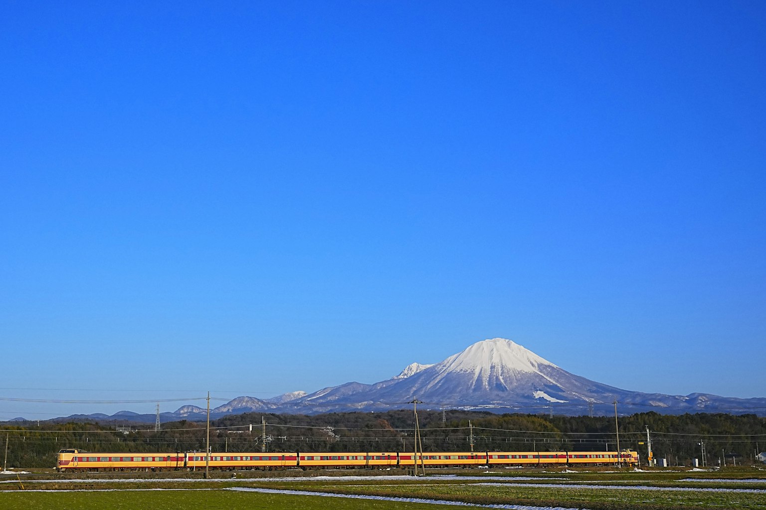 Montagna innevata con un treno giallo sotto un cielo blu