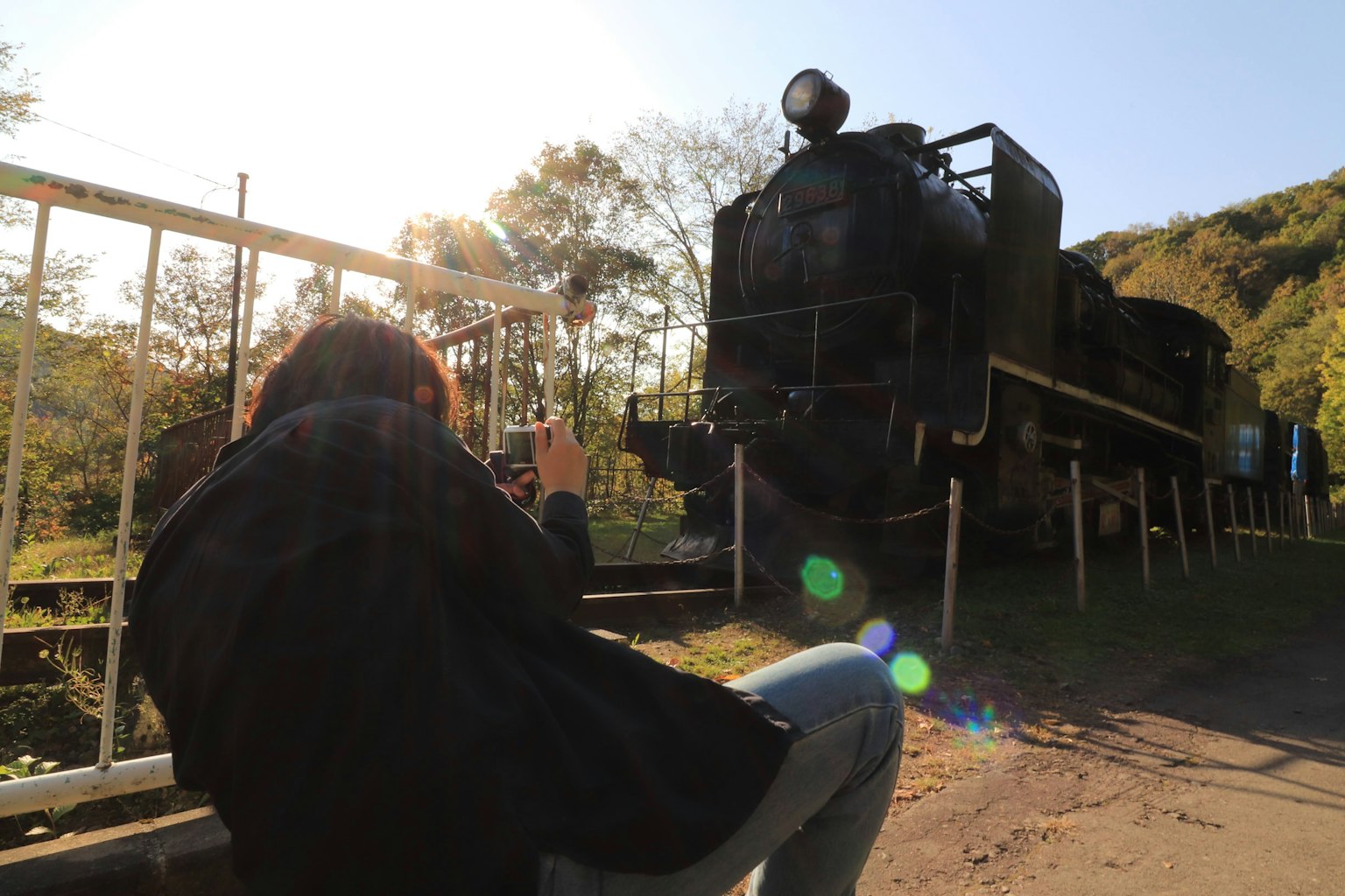 Silueta de una persona tomando una foto frente a una antigua locomotora de vapor con luz natural brillante