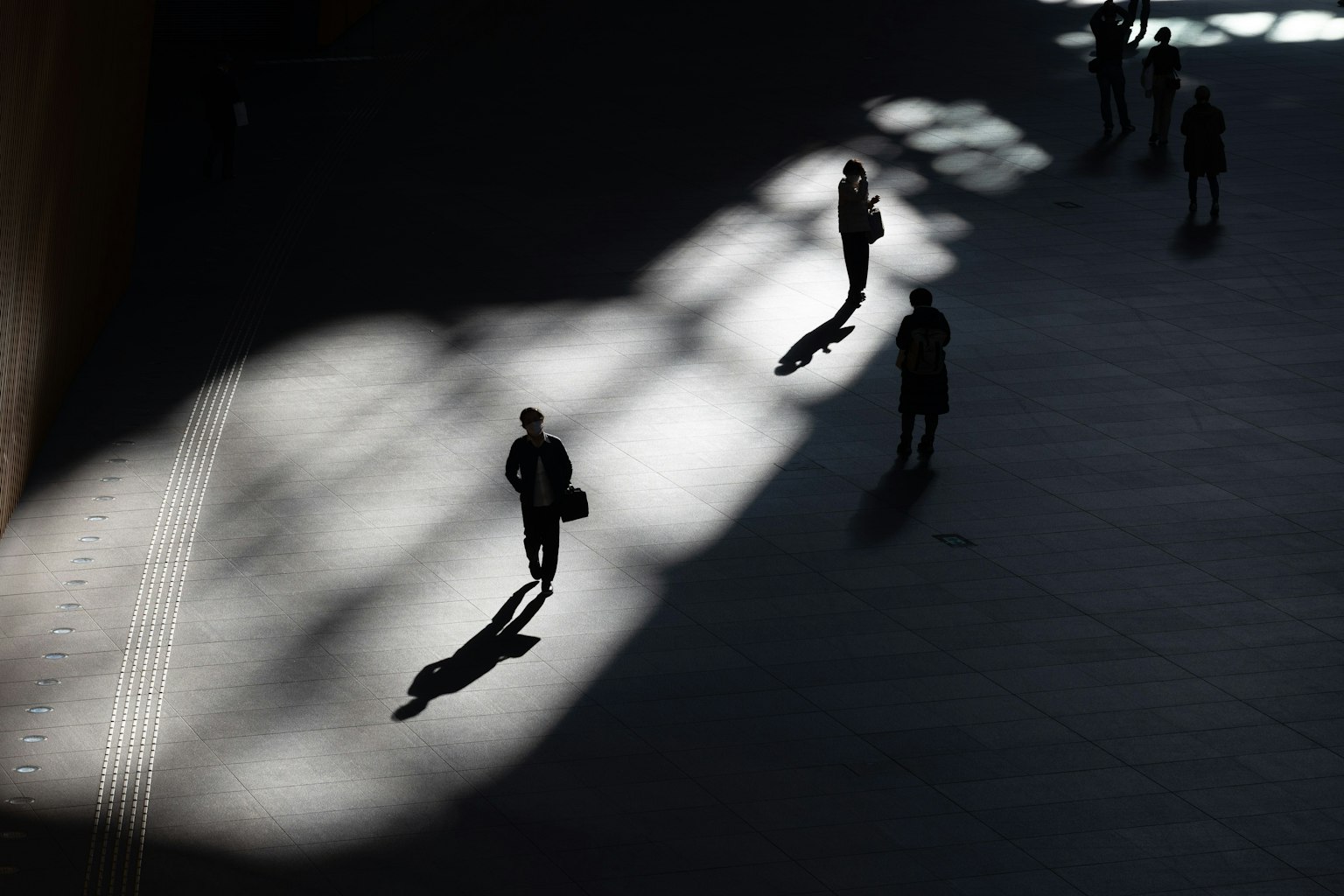 Siluetas de personas de negocios caminando en un espacio con sombras y patrones de luz