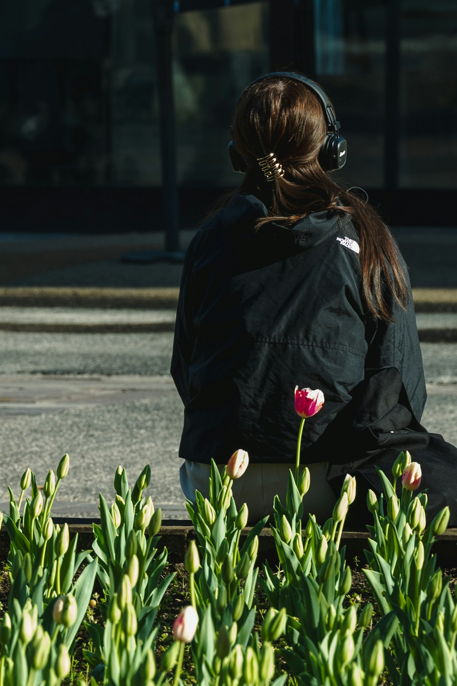 Femme portant des écouteurs assise de dos avec des fleurs de tulipes au premier plan