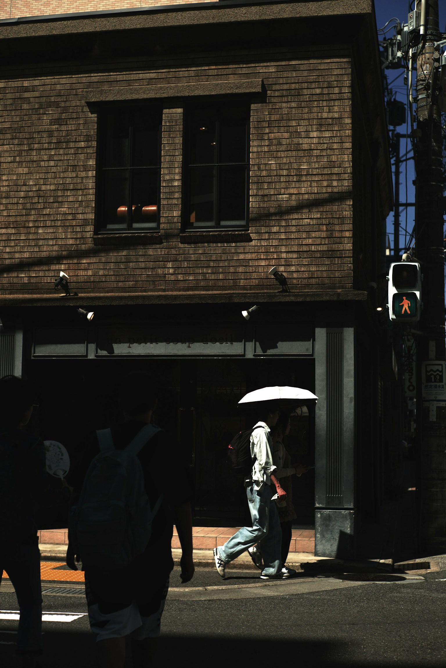 A person walking with an umbrella to shield from the sun in front of a brick building